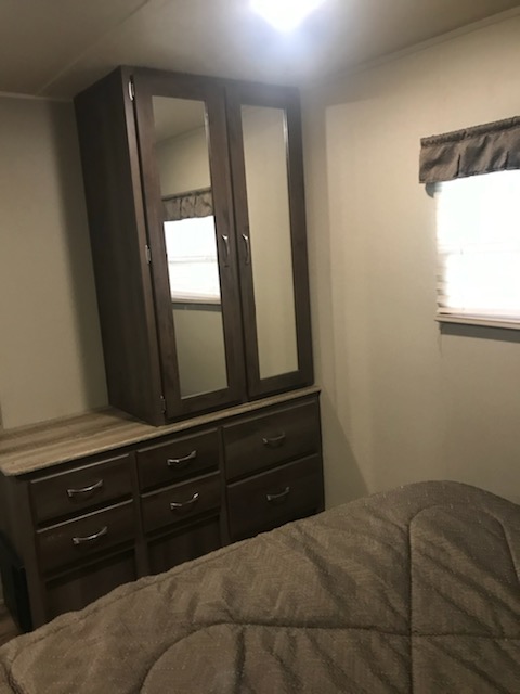 RV rental bedroom: dark wood wardrobe with mirrored doors atop a dresser, next to a window; part of a bed.. Forest River Puma 2016