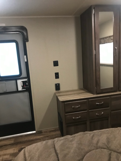 This RV rental bedroom features a compact dresser, mirrored cabinet, and an entrance door with a window.. Forest River Puma 2016
