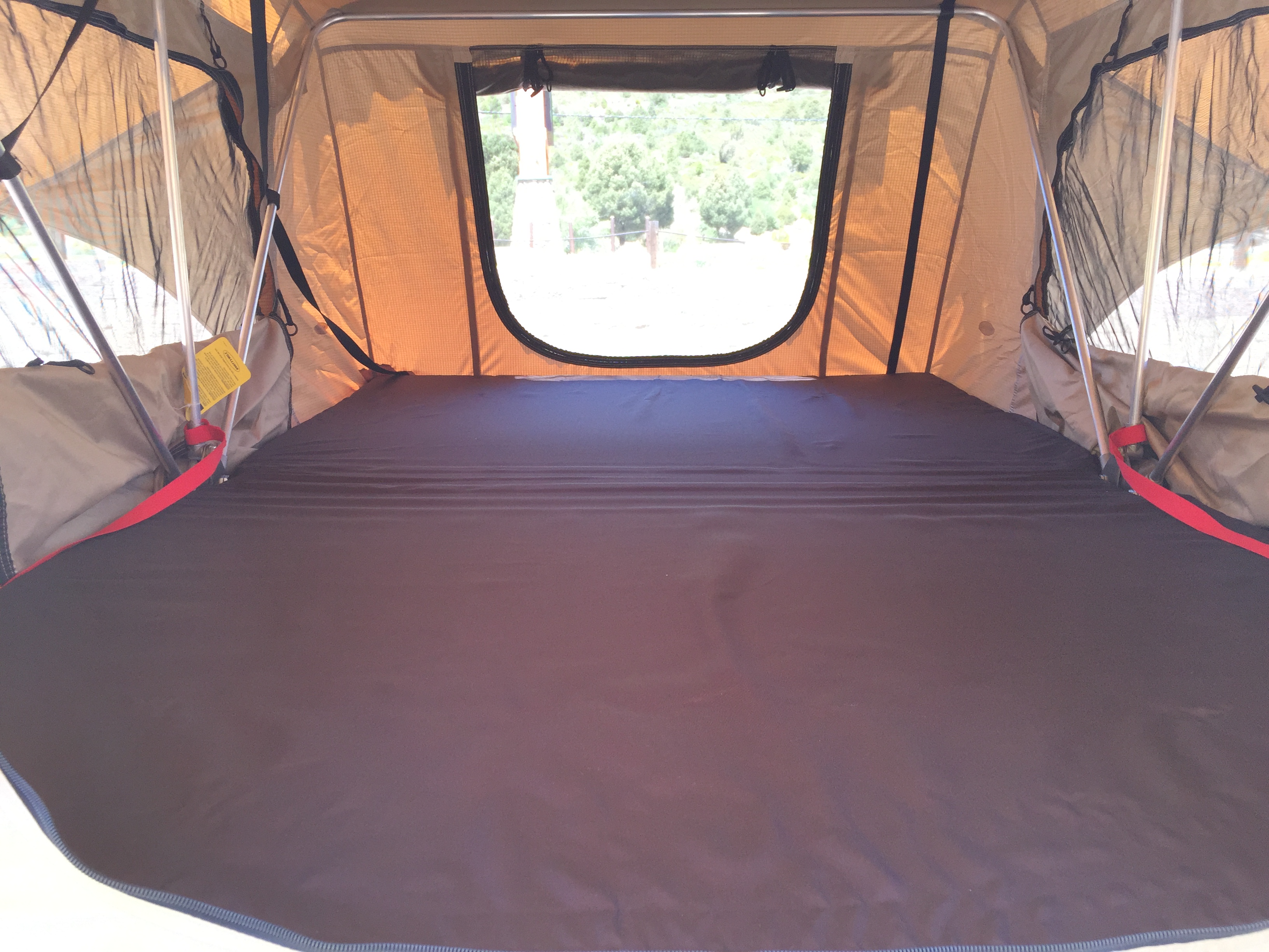 Interior of an rv rental rooftop tent, featuring a wide, flat dark mattress and a window looking out to nature.. Toyota Other 2008