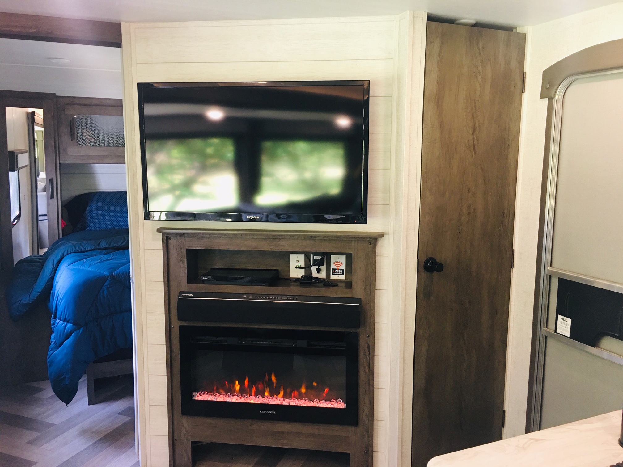 Cozy RV rental living area featuring a TV, electric fireplace, and a glimpse into the bedroom with a blue comforter.. Forest River Salem 2021