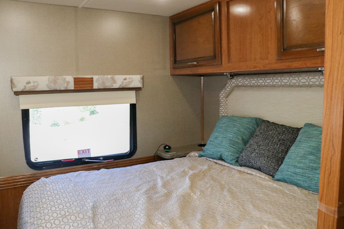 Comfortable RV rental bedroom with bed, colorful pillows, wooden cabinets, and window. Ideal for road trips and cozy stays.. Holiday Rambler Other 2017