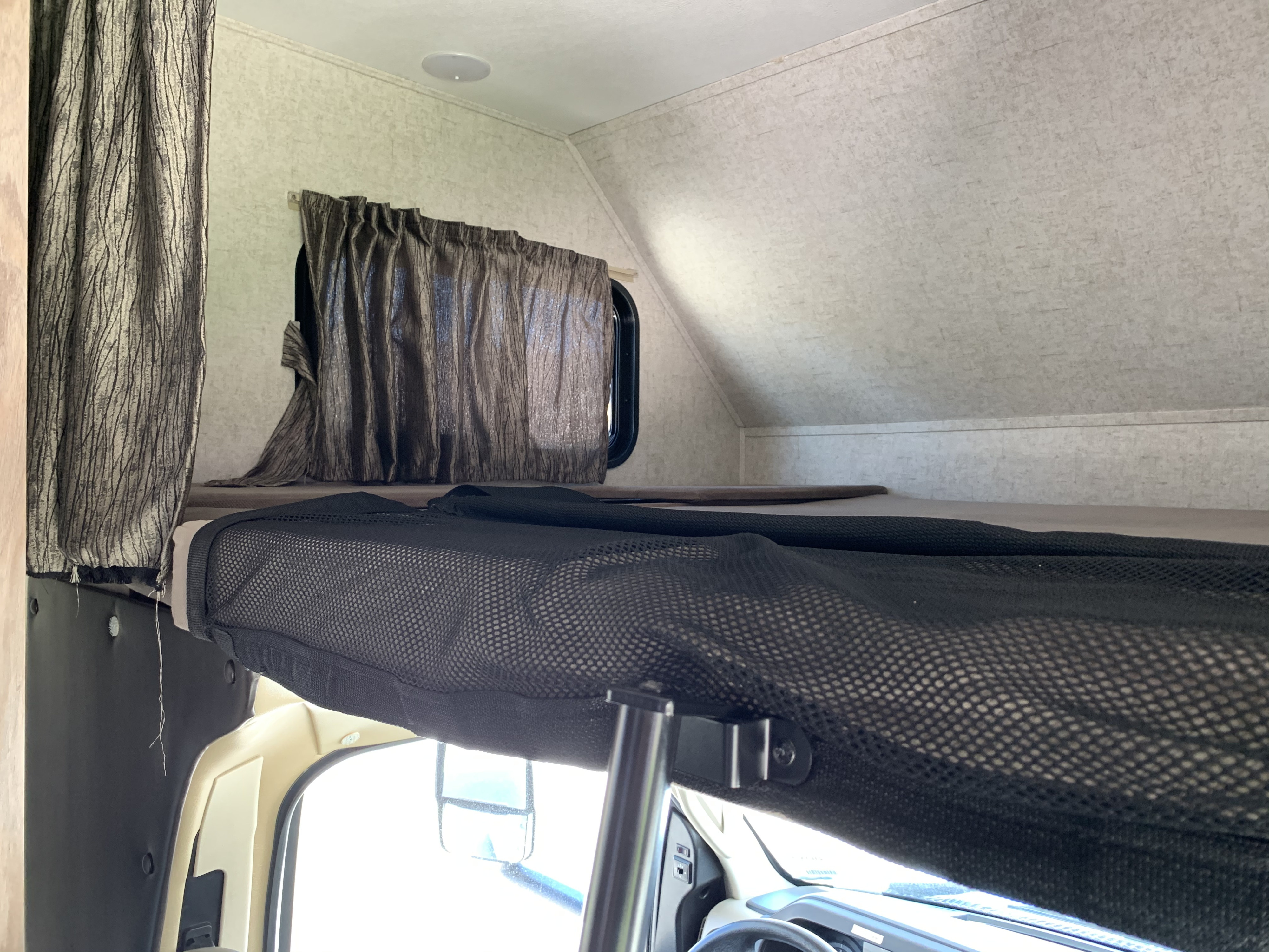 Inside an RV rental: a comfortable cab-over bunk bed with a mesh safety net and privacy curtains.. Forest River Sunseeker 2019