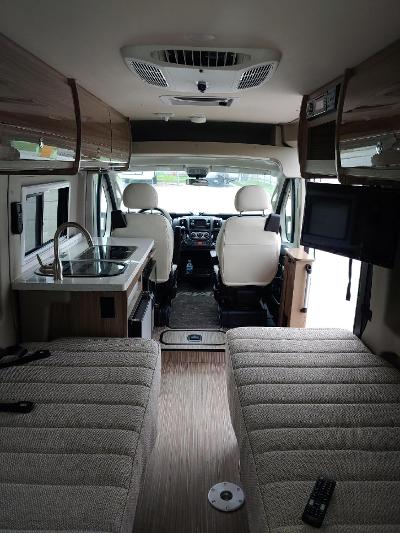 RV rental: Interior of a camper van showing cockpit, kitchenette, overhead cabinets, and twin beds.. Winnebago Travato 2019