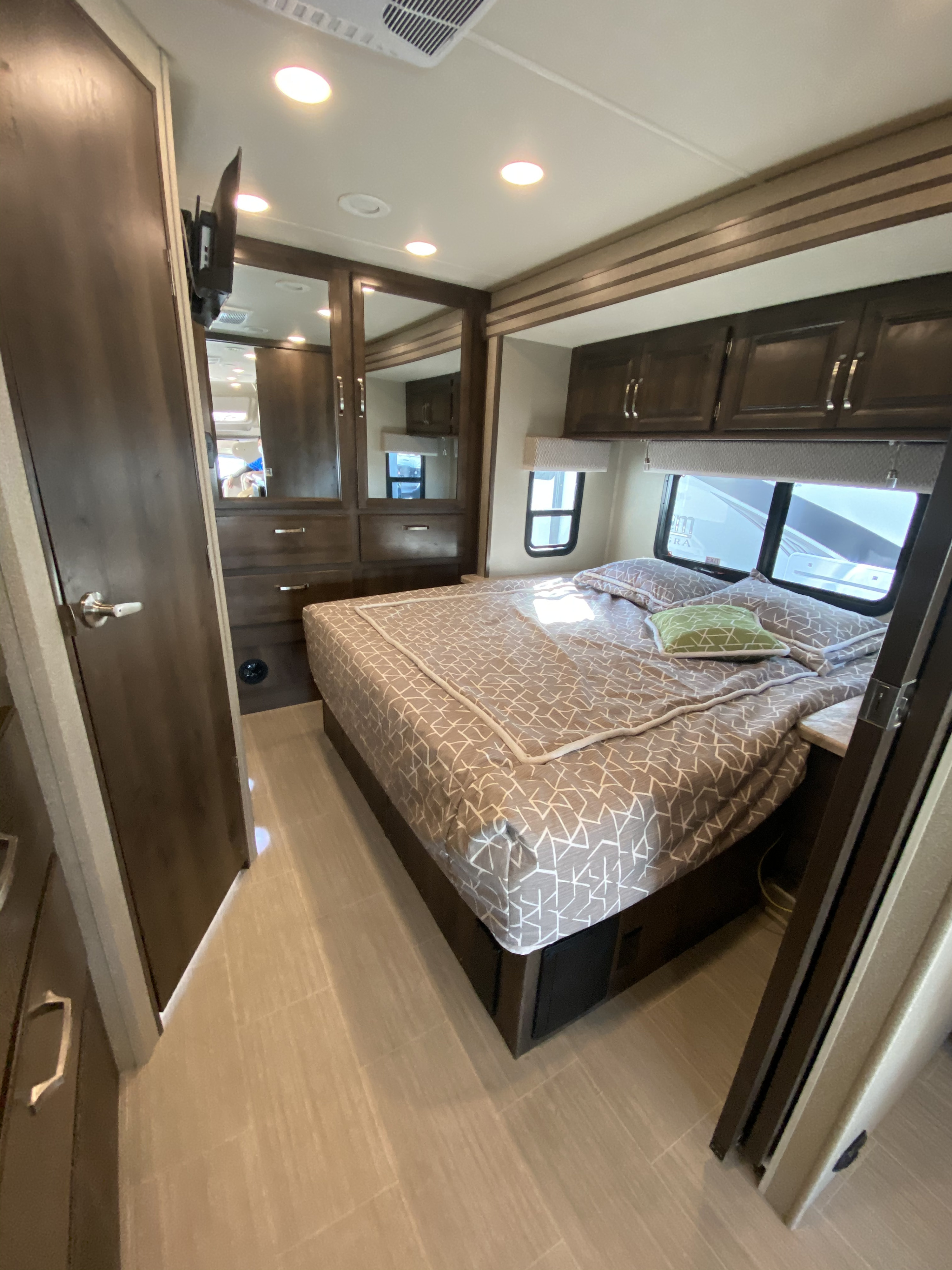 Comfortable RV rental bedroom with patterned bed, ample storage via cabinets/wardrobe, and natural light from windows.. Entegra Coach Esteem 2020