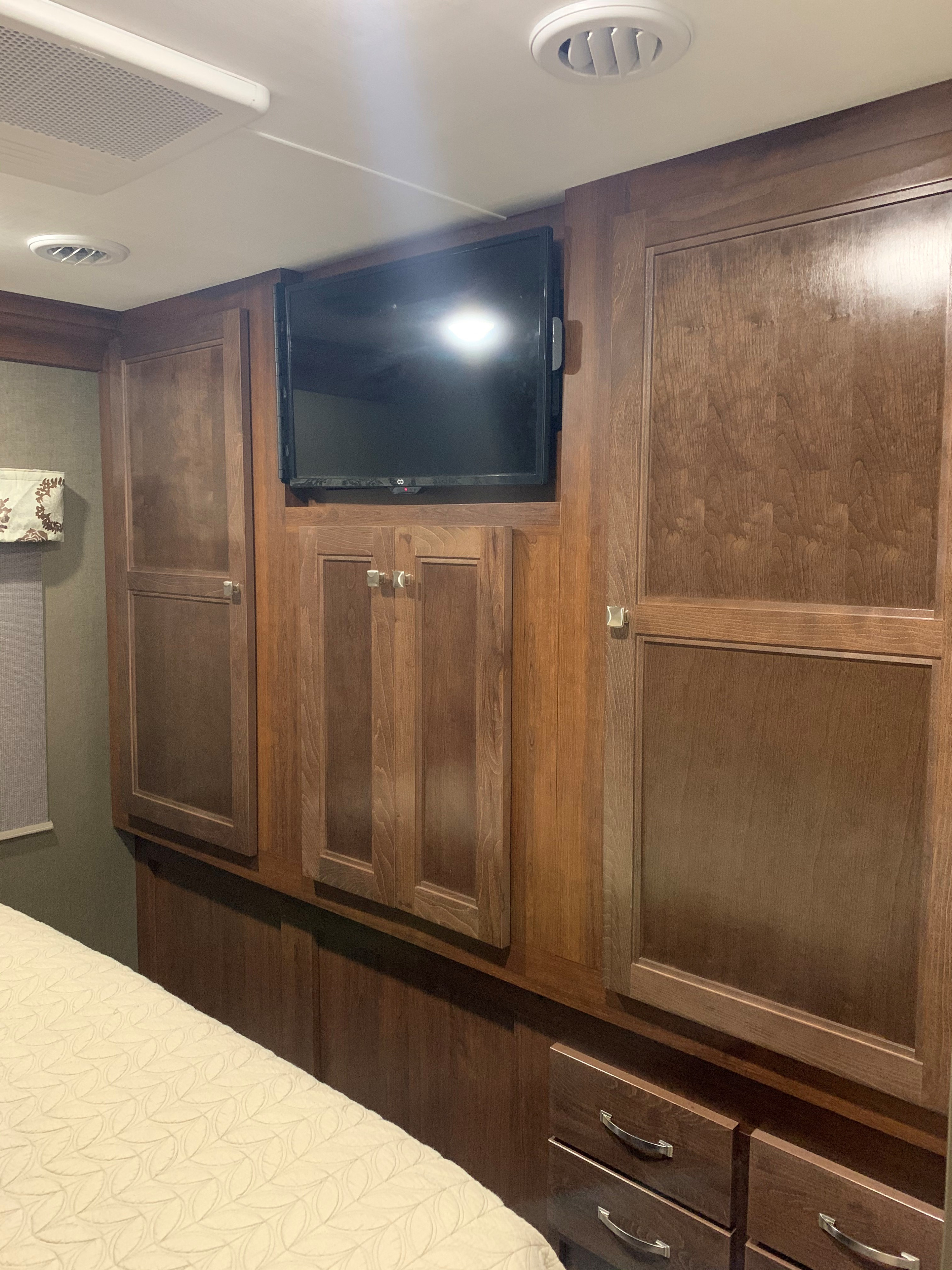 RV rental bedroom featuring dark wood cabinets, a mounted TV, and ceiling vents above a patterned bedspread.. Forest River Forester 2020