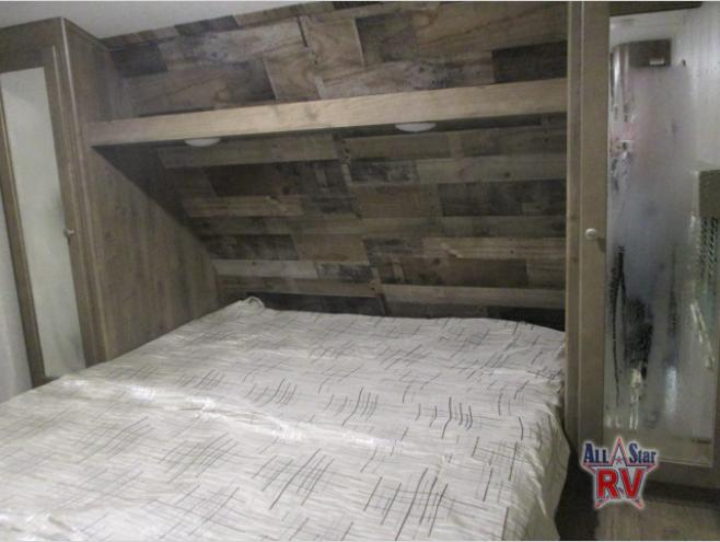 A clear view of an RV rental bedroom, showing a patterned bed, rustic wood walls, and a nearby frosted shower door.. Dutchmen Aspen Trail 2019