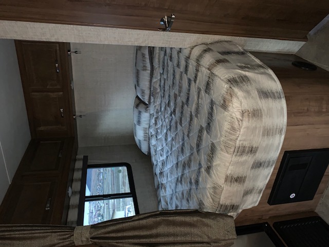 RV rental bedroom: cozy interior with a patterned bed, overhead cabinets, and window view.. Gulf Stream Conquest 2020