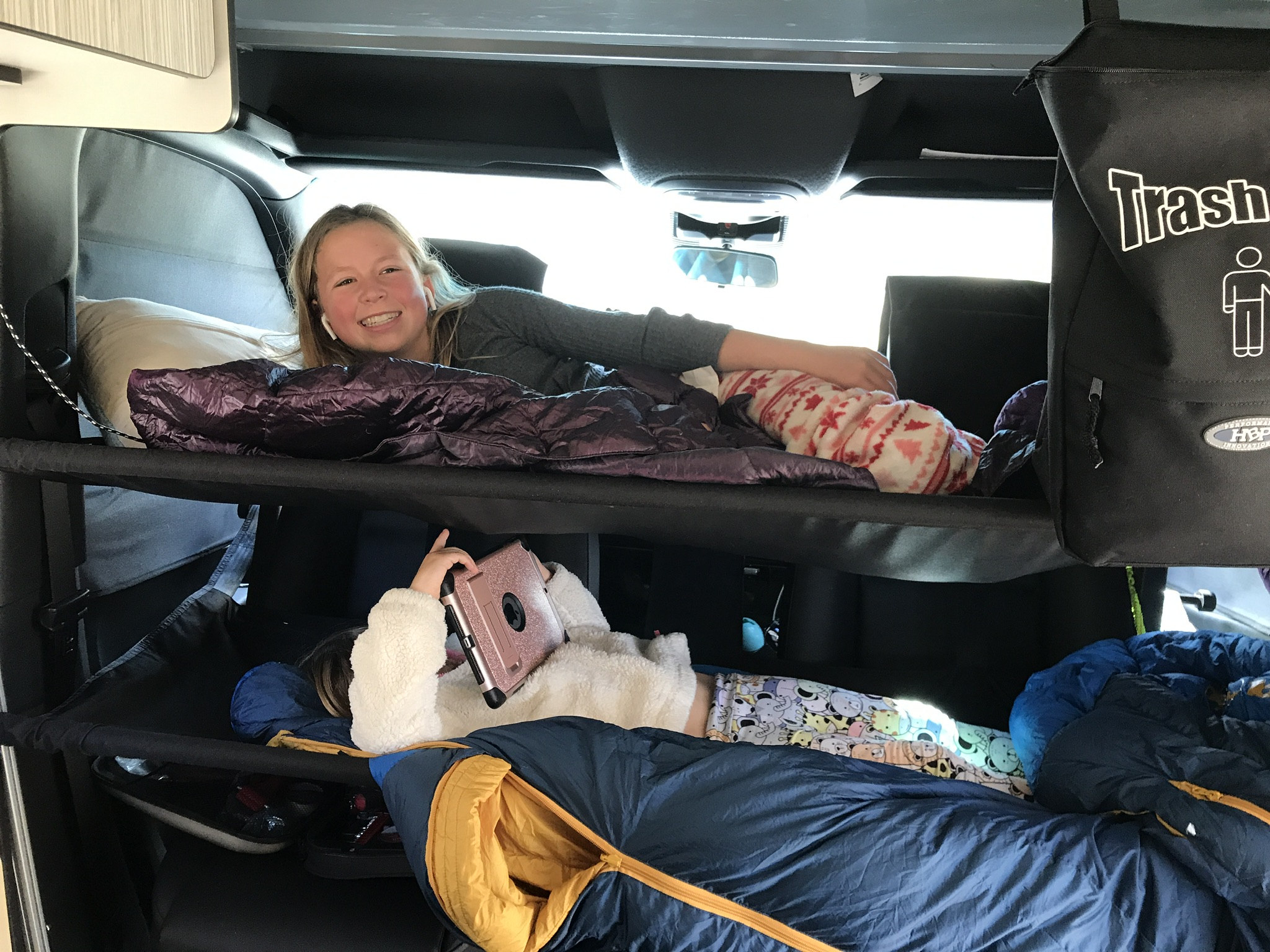 Two girls relaxing in bunk beds within an RV rental. Top girl smiles, bottom uses tablet. Ideal for road trip camping.. Mercedes Sprinter 2020