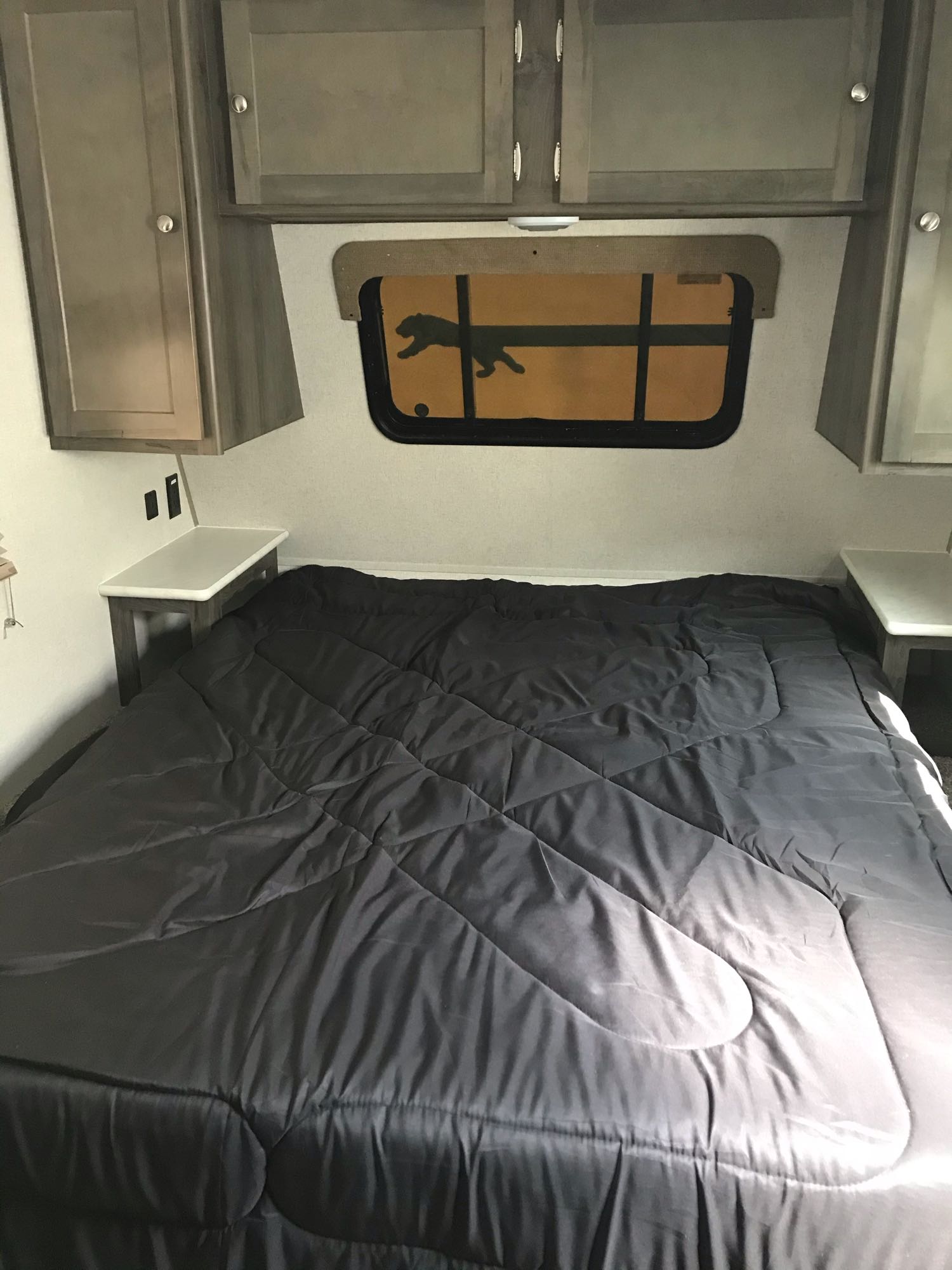 Comfortable RV rental bedroom featuring a large bed with dark comforter, overhead cabinets, and a unique window design.. Coachmen Clipper 2020