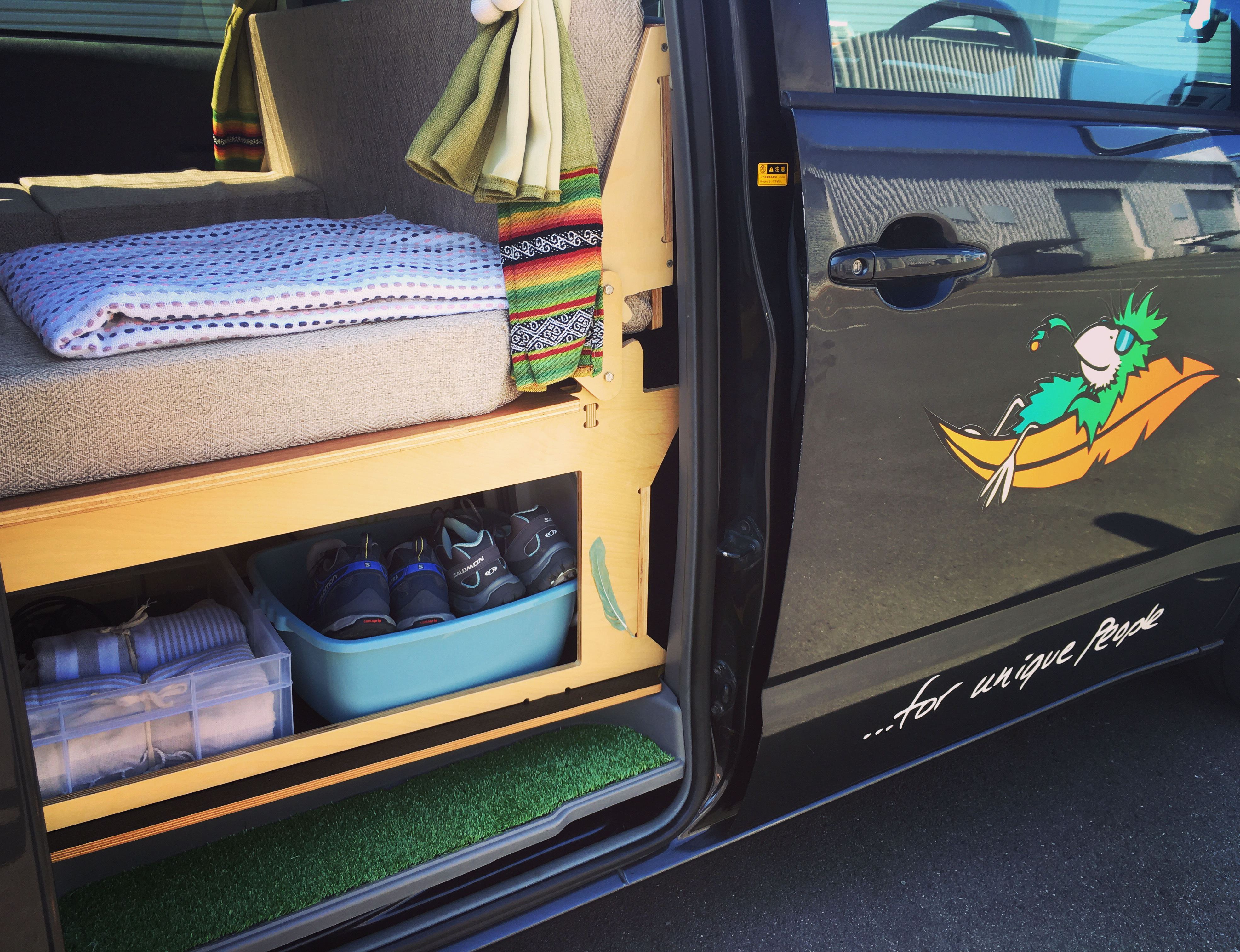 Customized RV rental interior with bed, smart storage for shoes and towels, and a fun parrot graphic on the door.. Toyota Voxy 2006