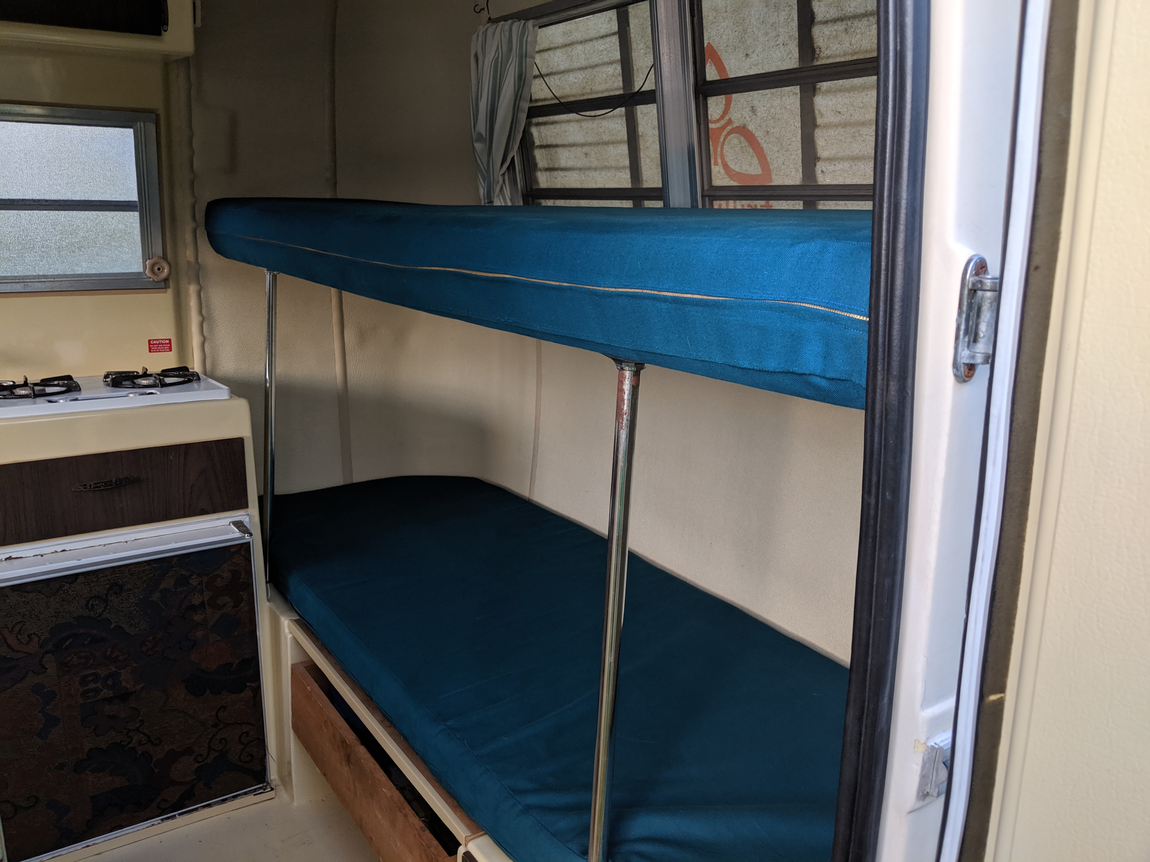 Cozy RV rental interior with bunk beds, compact kitchen, and windows, ideal for a comfortable mobile adventure.. Trillium Rv Other 1981