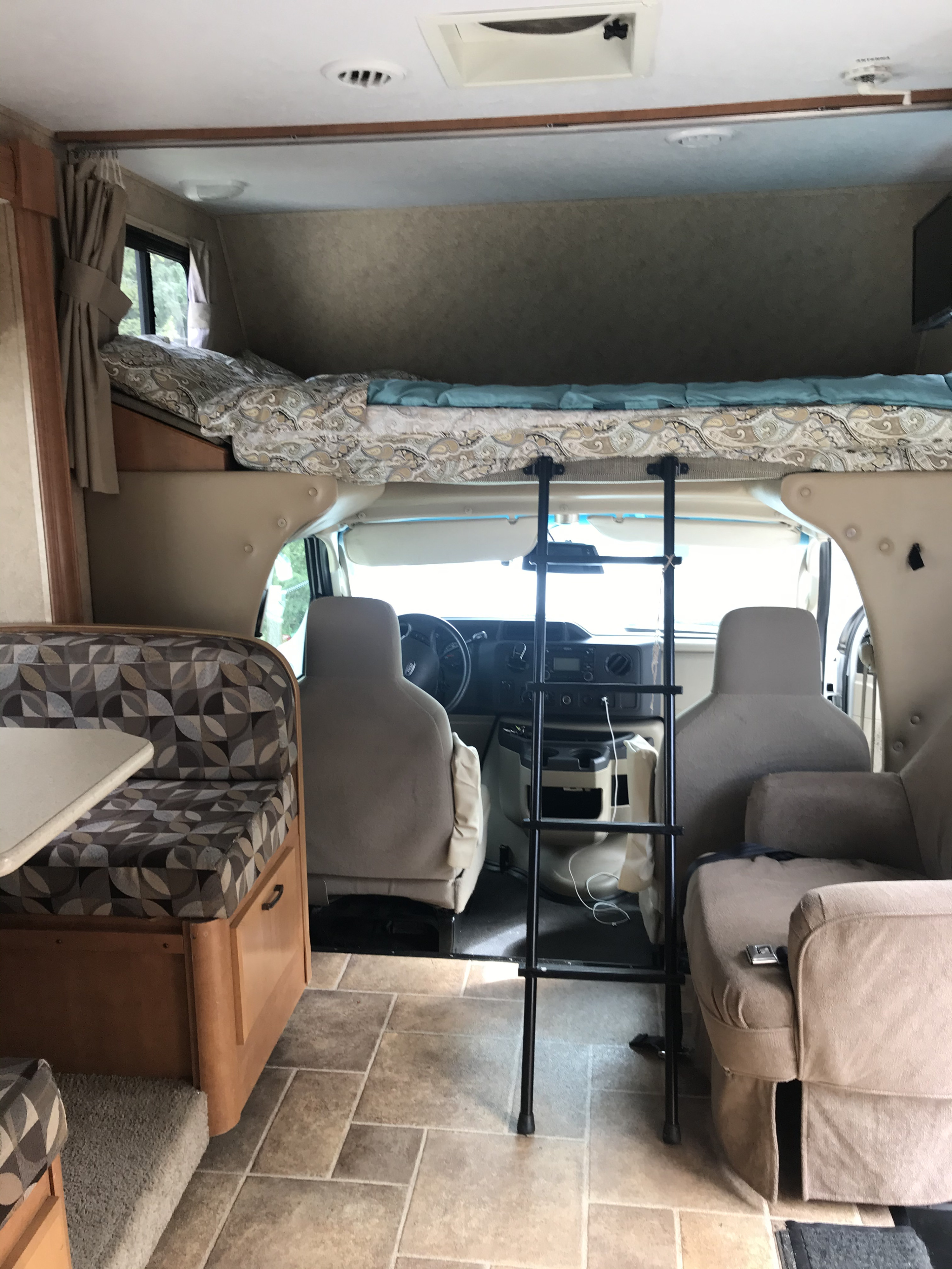 Interior of an RV rental: view from rear, showing cab-over bed, driver's area, dinette (left), & armchair (right).. ForestRiver Sunseeker 2012