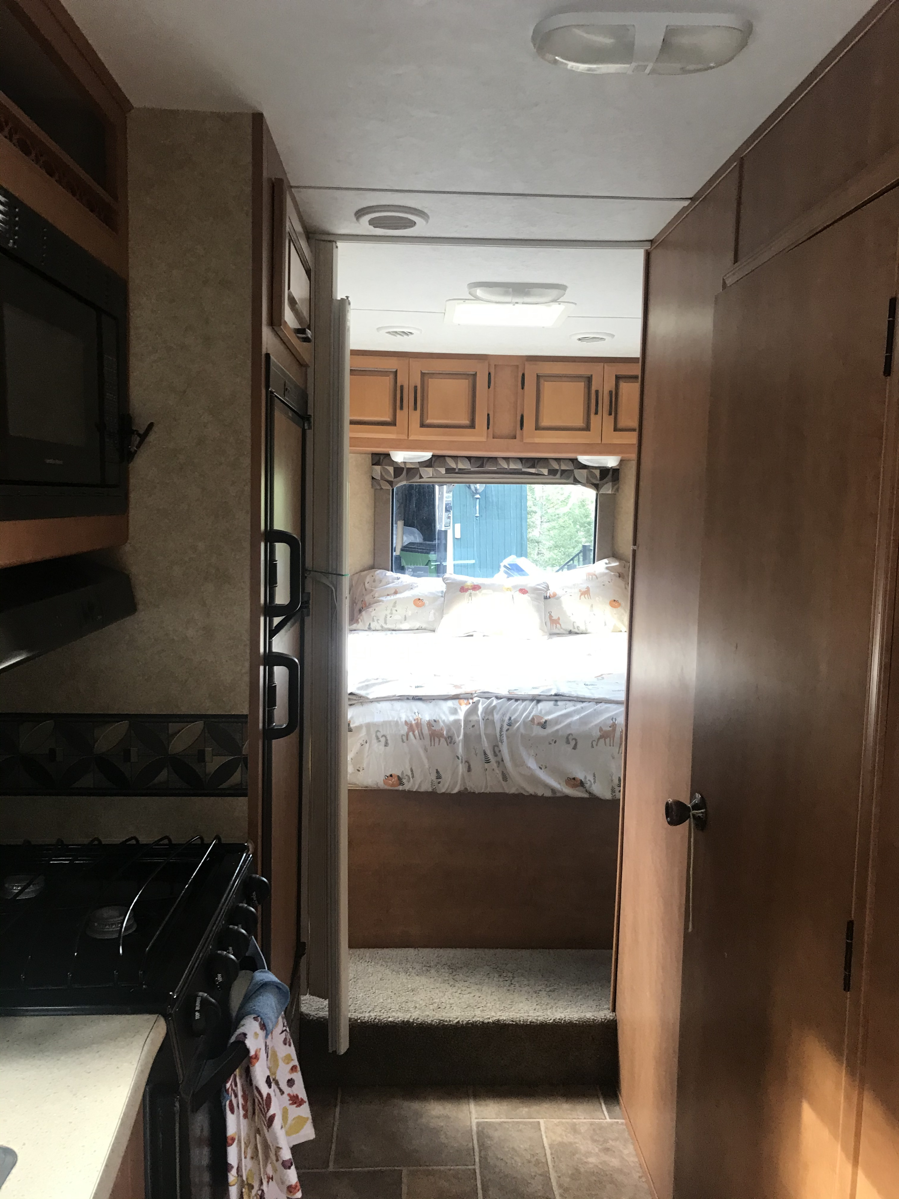 Inside an RV rental: kitchen appliances on left, hallway to raised bedroom with patterned bedding.. ForestRiver Sunseeker 2012