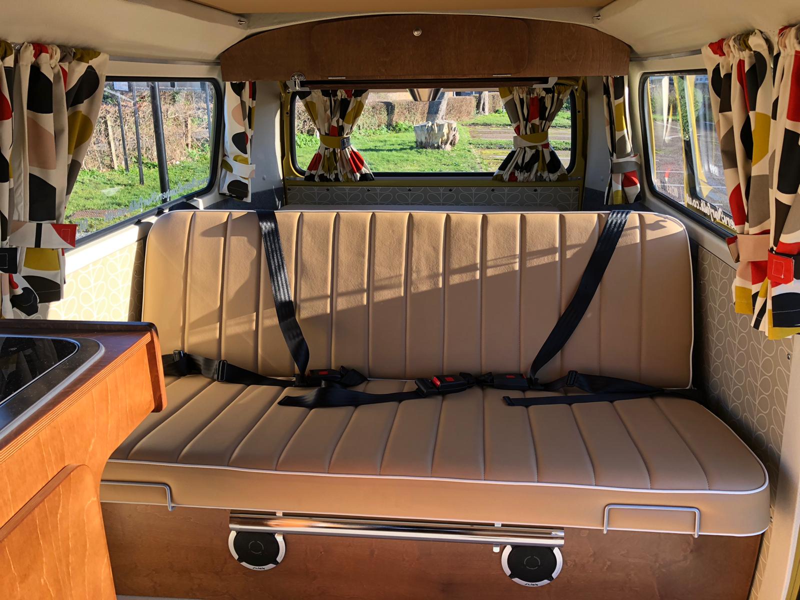 Retro camper van rv rental interior: tan bench seat with seatbelts, bright curtains, view outside, and built-in speakers.. Volkswagen 2.0L T2 Late Bay 1975