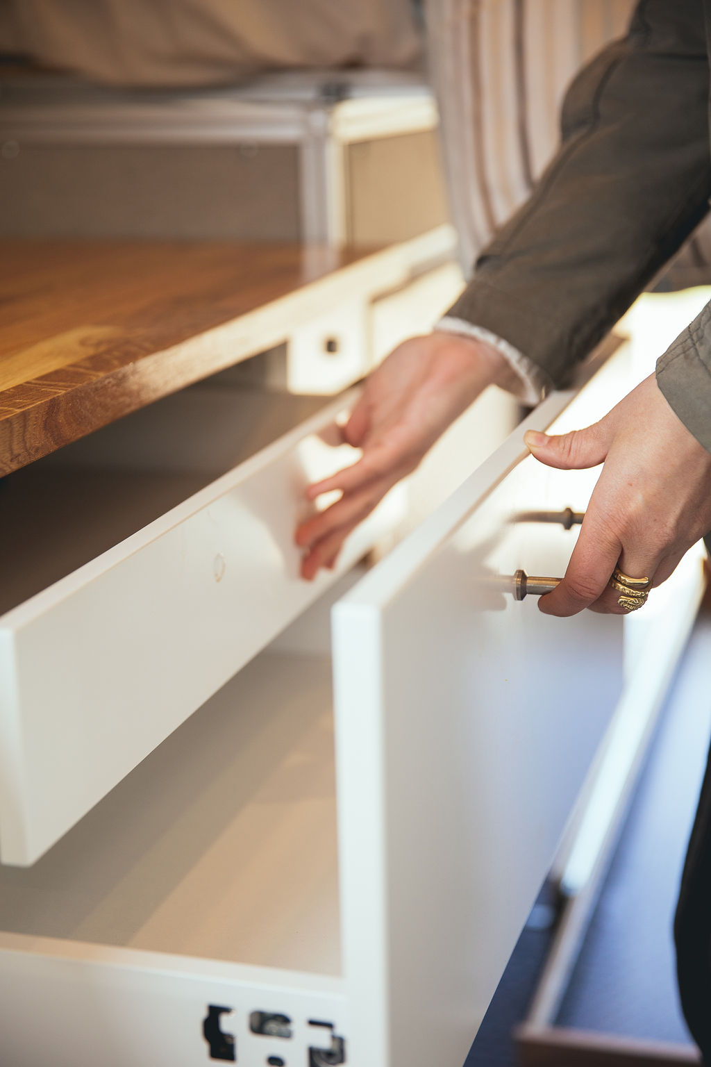 Hands open white storage drawers in an RV rental. These compact built-in compartments offer convenient interior organization.. Mercedes-Benz Sprinter 2018