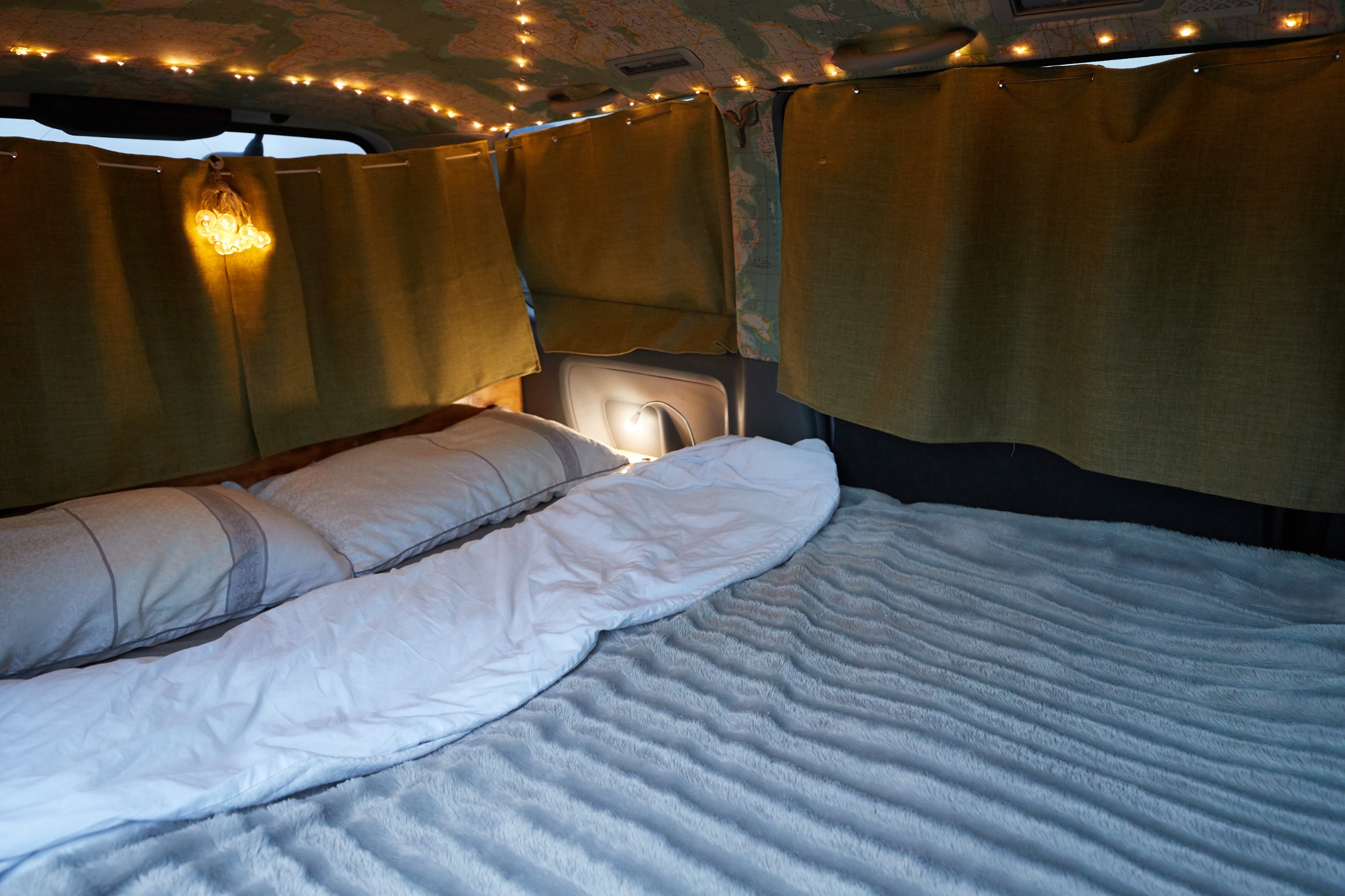 Cozy RV rental interior with comfortable bed, string lights on map ceiling, and olive green privacy curtains.. Toyota Voxy 2007