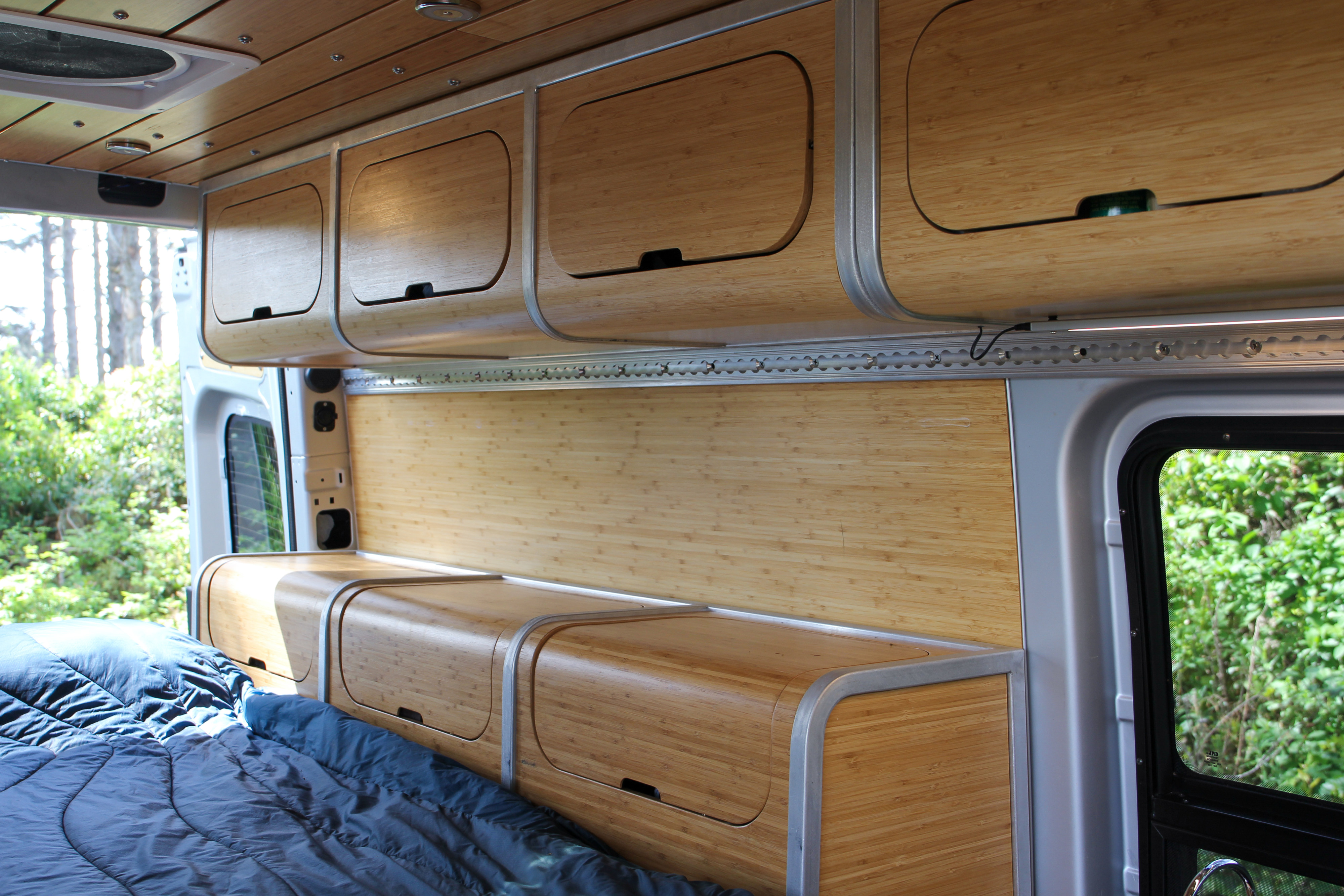 An RV rental interior with sleek bamboo cabinets, bed, and wall panels, offering a cozy mobile living space.. Mercedes-Benz Sprinter 2018