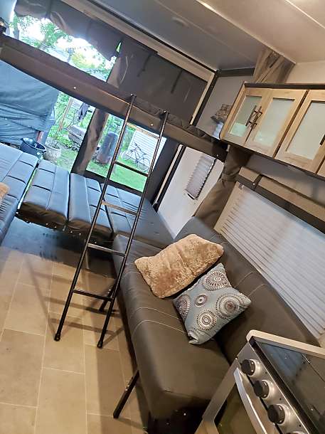 Inside this RV rental, an open ramp door reveals the outdoors, alongside a bunk bed, sofas, and a partial kitchen view.. Palomino Puma 2020