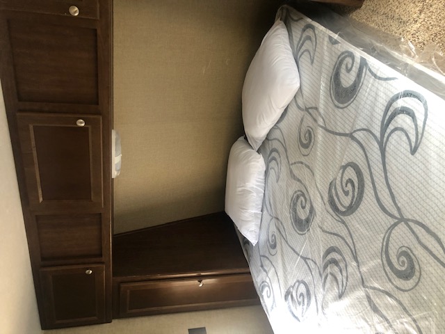 Cozy RV rental bedroom interior with a new, plastic-wrapped mattress, white pillows, and dark wood storage cabinets.. Keystone RV Hideout Luxury 2015