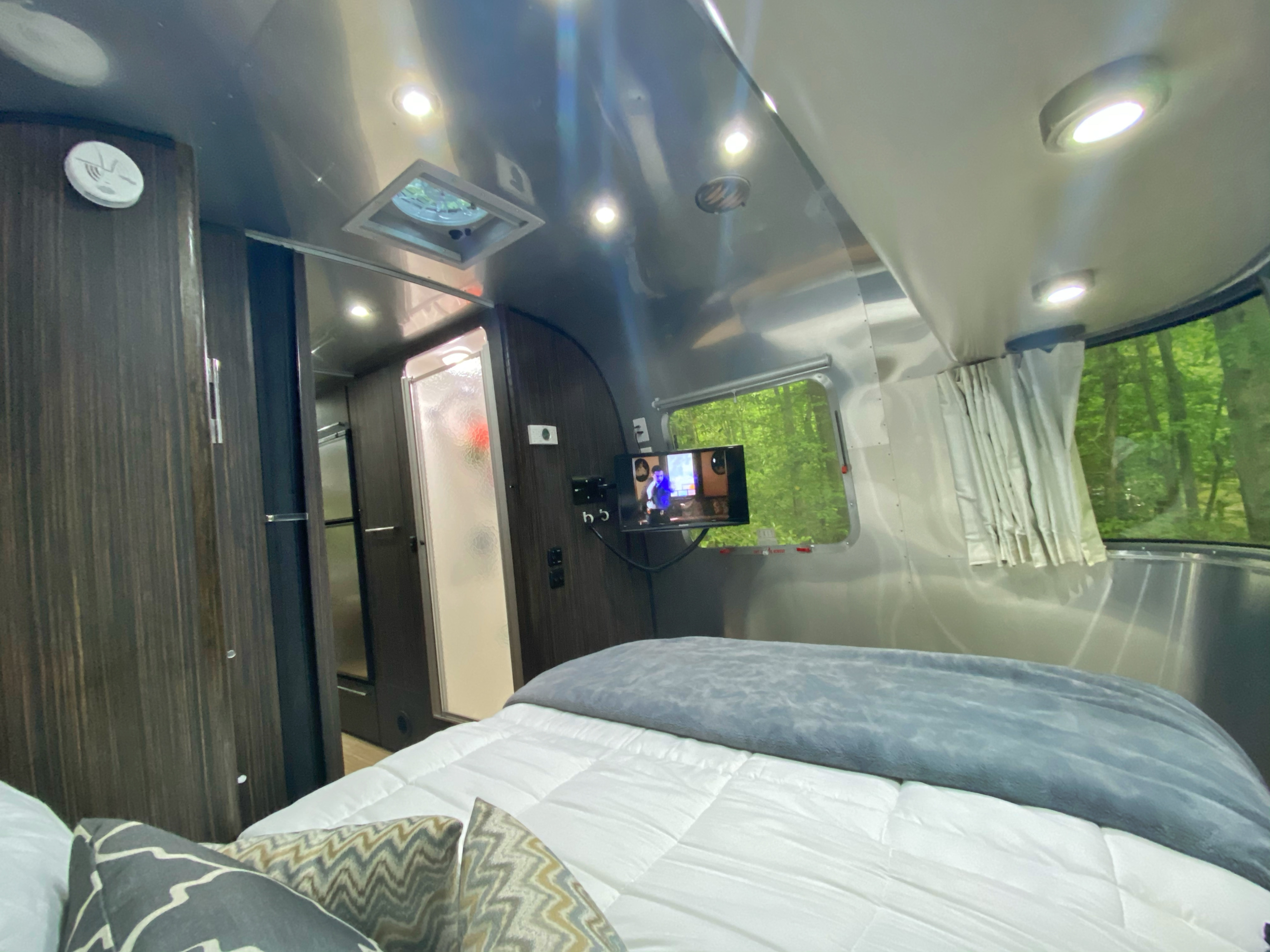 RV rental: A bright Airstream interior showing the bedroom with a comfortable bed, mounted TV, shower, and forest window view.. Airstream International 2019