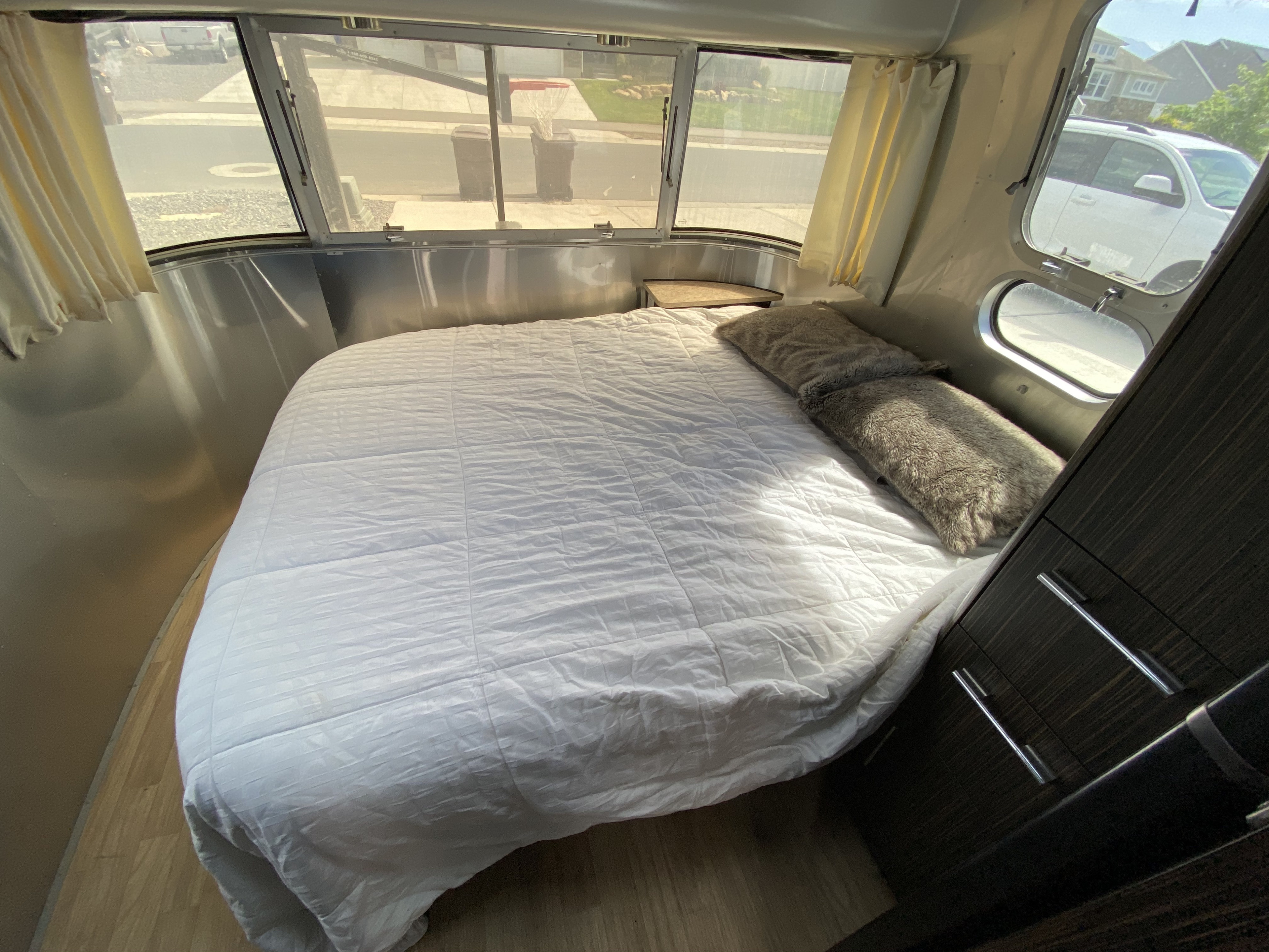Inside an RV rental: a bright, comfortable bedroom with a white bed, plush pillows, and a street view.. Airstream International 2015