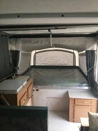 Discover the cozy interior of this RV rental pop-up camper! Features a spacious bed, wooden cabinets, and curtained windows for your camping trips.. Coleman Destiny Cheyenne 1998