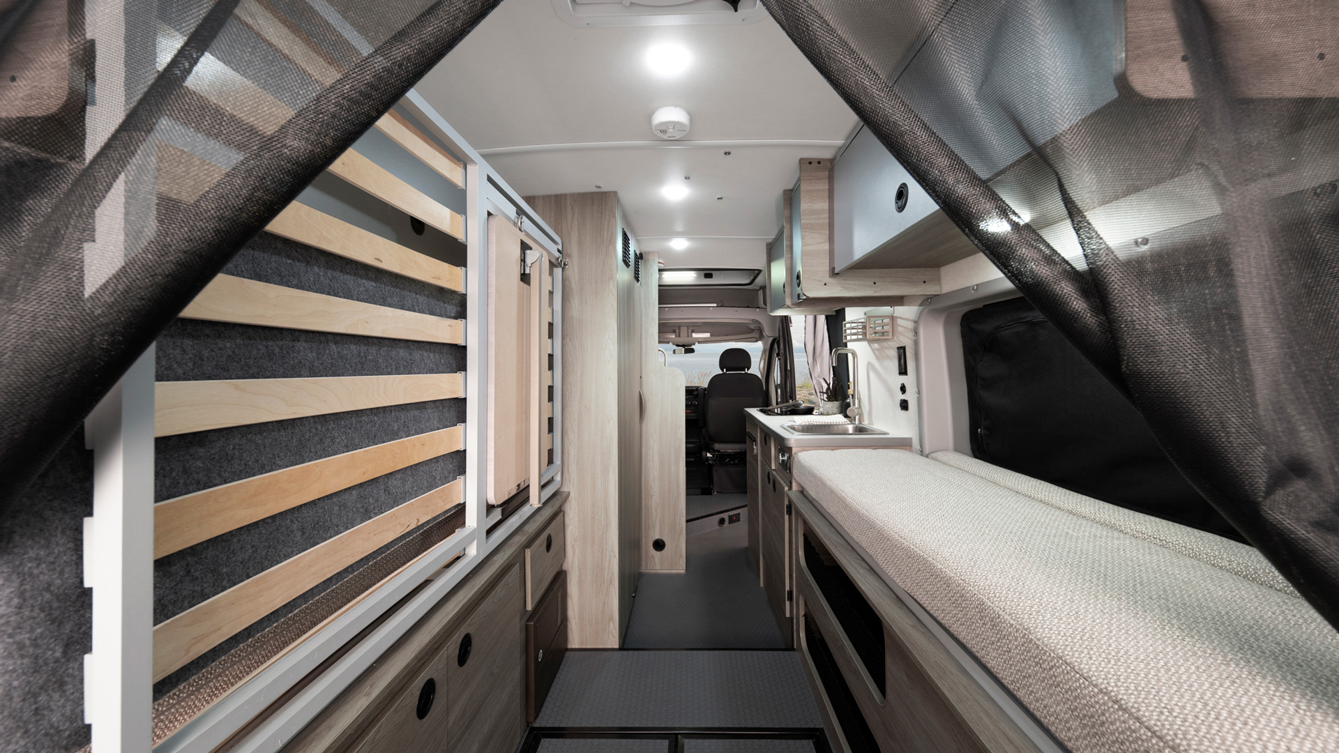 Inside a compact rv rental camper van, showing a kitchen sink, cushioned bench/bed, and convertible slat bed system.. Winnebago Solis 2021