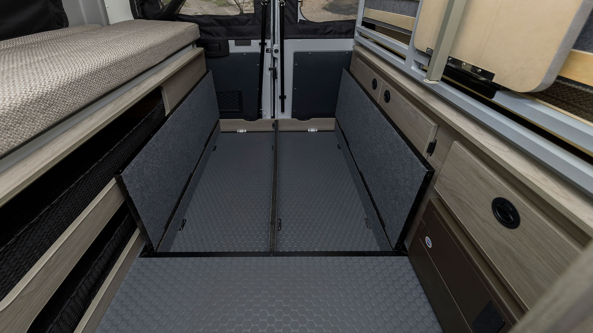 RV rental interior showcases a cozy beige bed, light wood cabinets, and a versatile gray floor with two deep storage compartments.. Winnebago Solis 2021