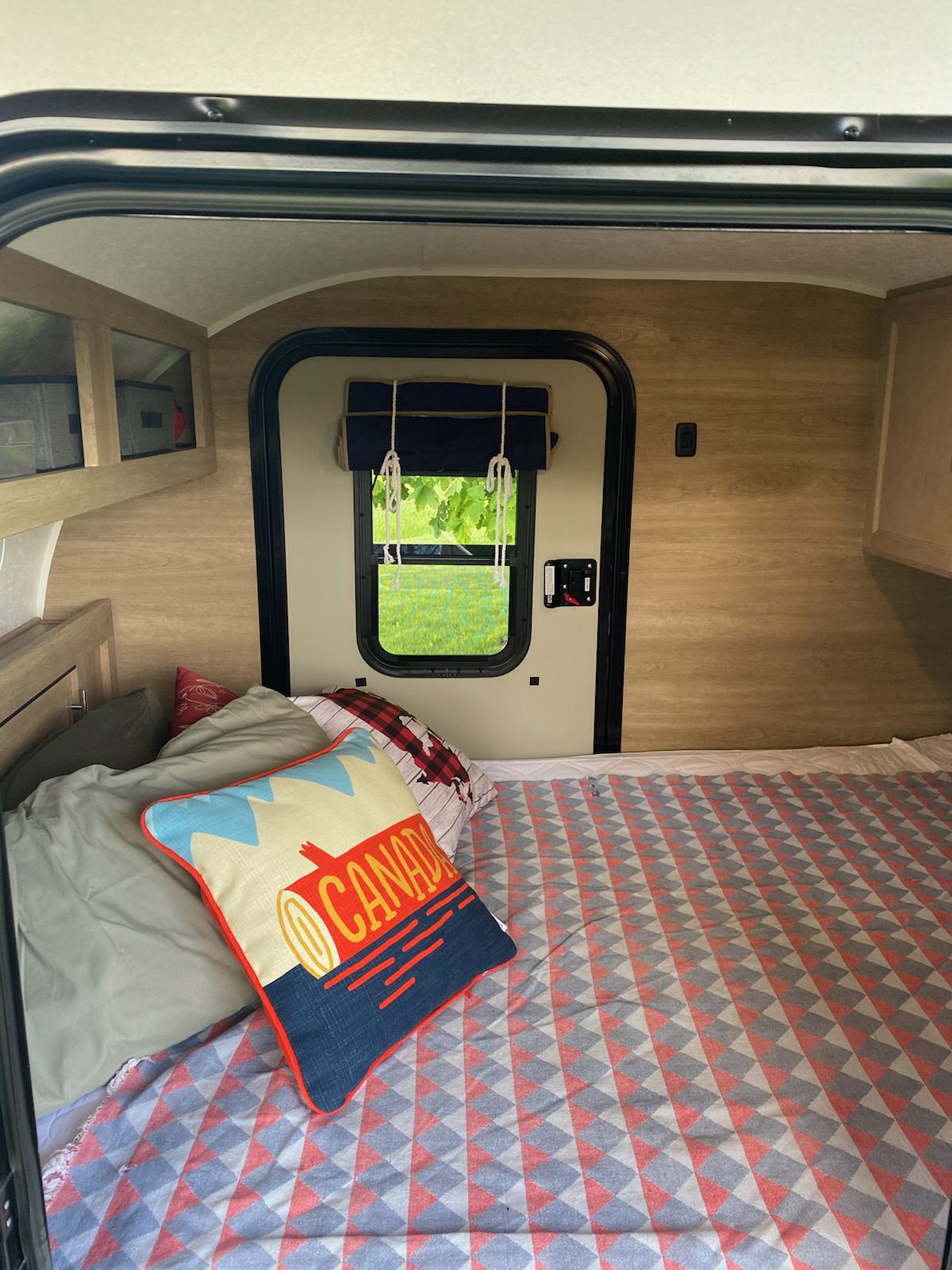 Cozy interior of an RV rental, featuring a bed with a vibrant blanket & Canada pillow, and a view of nature.. Braxton Creek Bushwhacker 2020