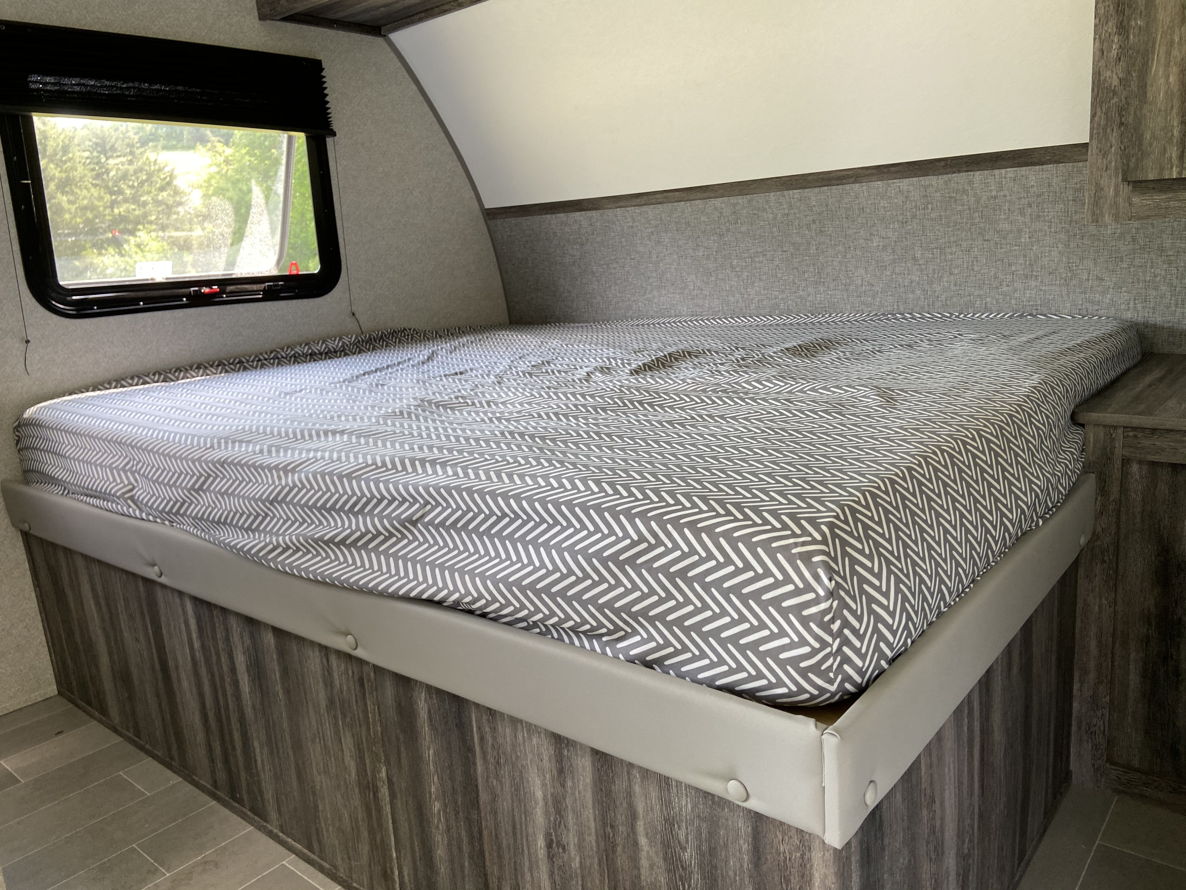 Experience comfort in this rv rental! View of the main bed area, showing its patterned sheet, window, and textured walls.. Forest River 2020 Wildwood 2020