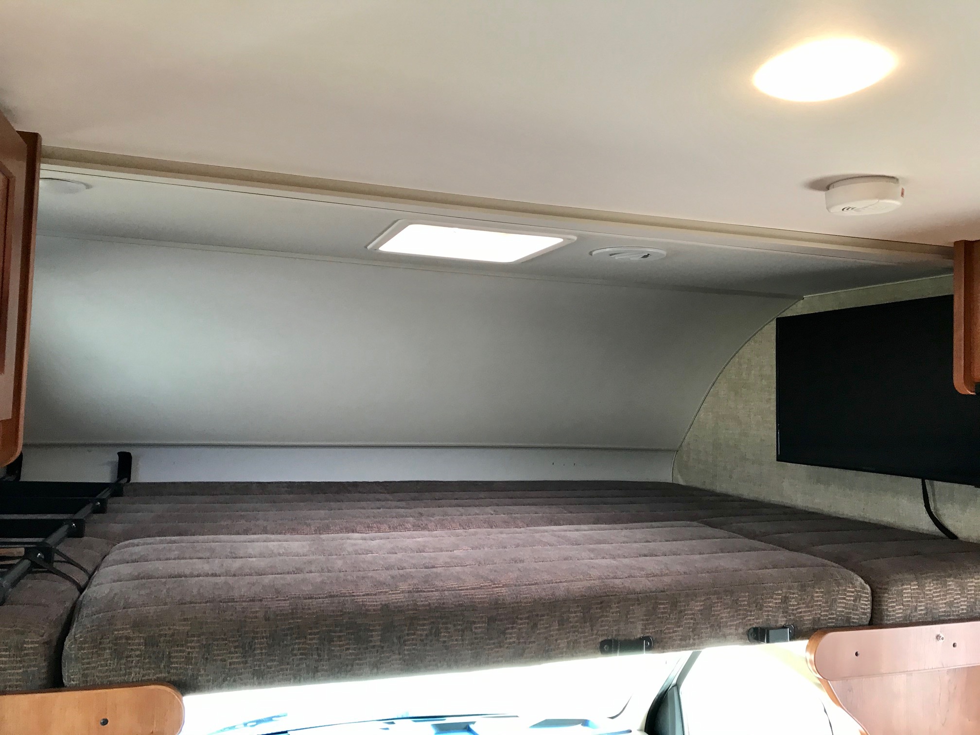 RV rental interior: cozy cab-over bunk bed with patterned cushions, TV, ceiling lights, and smoke detector for a comfy stay.. Winnebago Minnie Winnie 2019