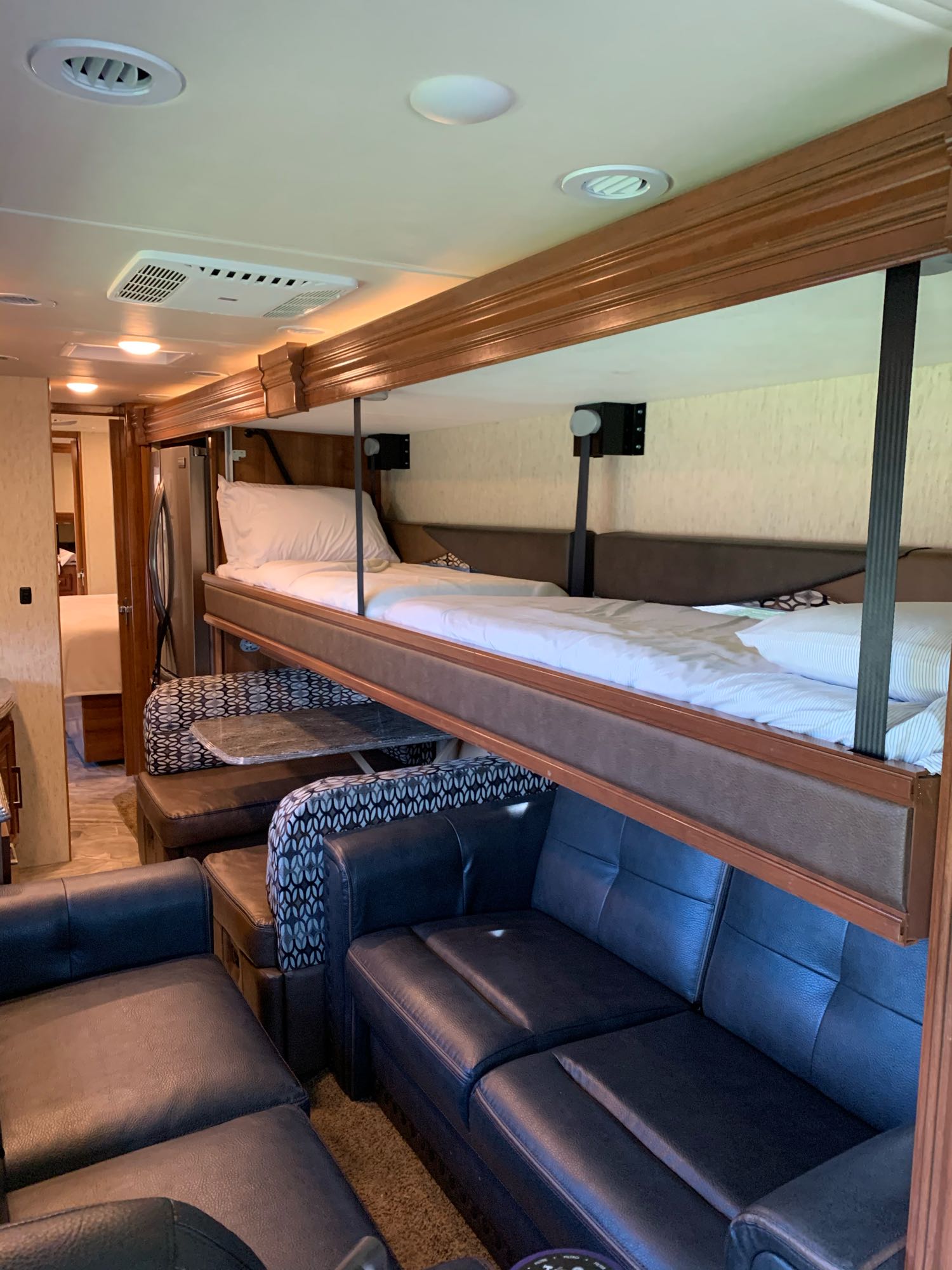 Inside an RV rental: versatile living area with dark leather sofas, a dinette, and clever pull-down bunk beds for extra sleeping.. Coachmen Sportscoach 2018