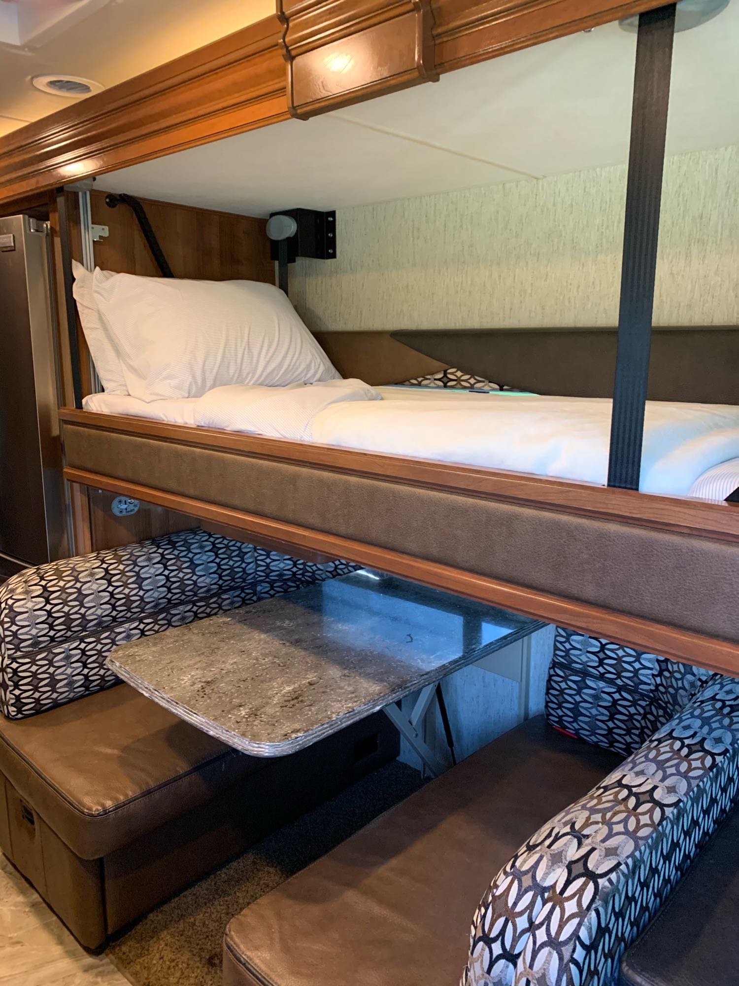Inside an rv rental, a drop-down bunk bed with white bedding is suspended over a dinette, offering clever space-saving for travelers.. Coachmen Sportscoach 2018