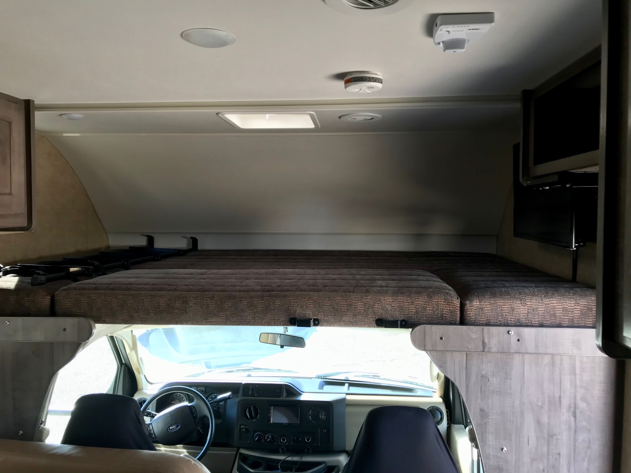 View inside an rv rental, showing the cab-over bunk bed, front cockpit area, and overhead TV.. Winnebago Minnie Winnie 2019