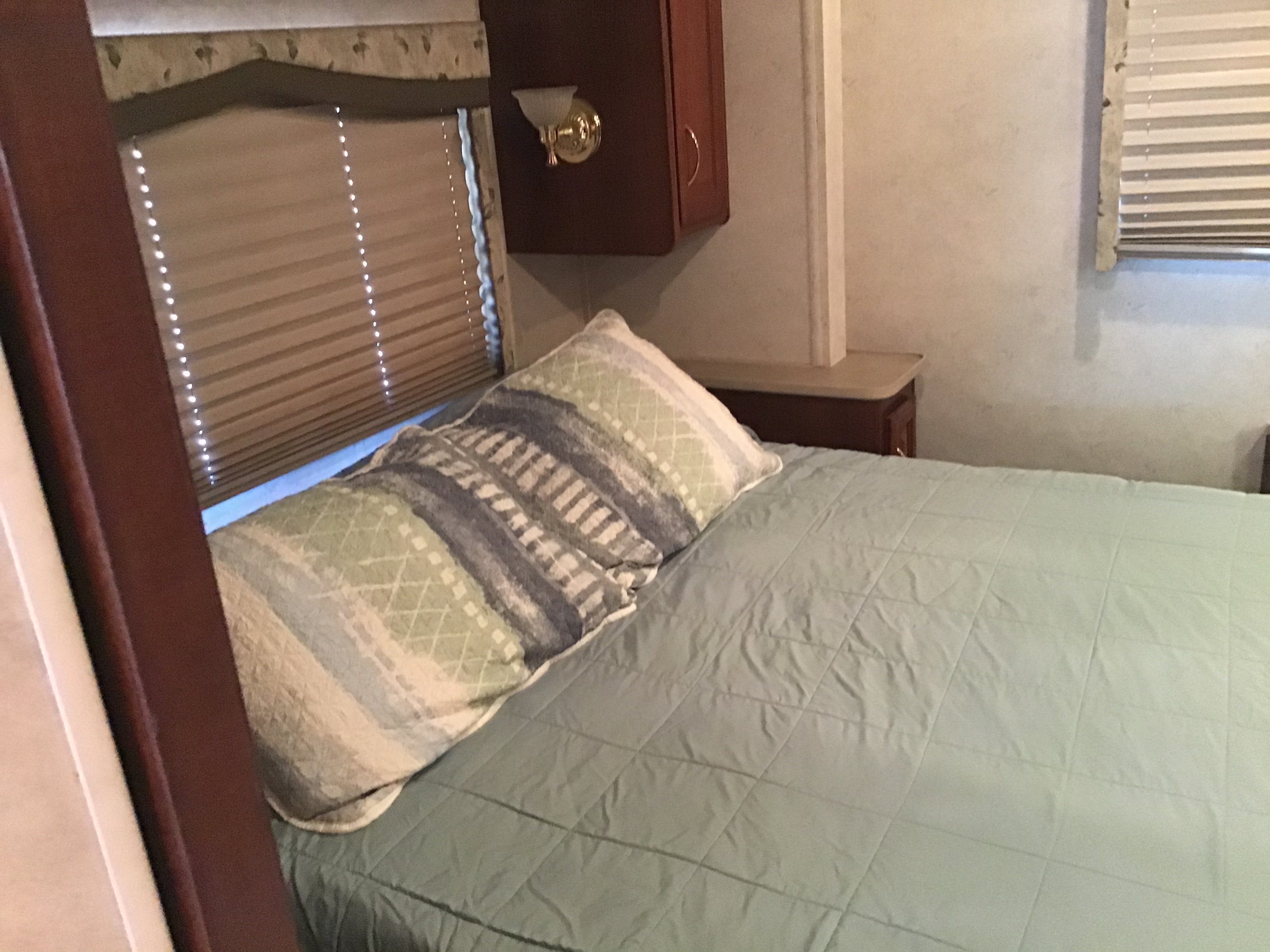 RV rental bedroom: a cozy bed with a light blue quilted comforter and patterned pillow, featuring window blinds and a cabinet.. Fleetwood Bounder 2002