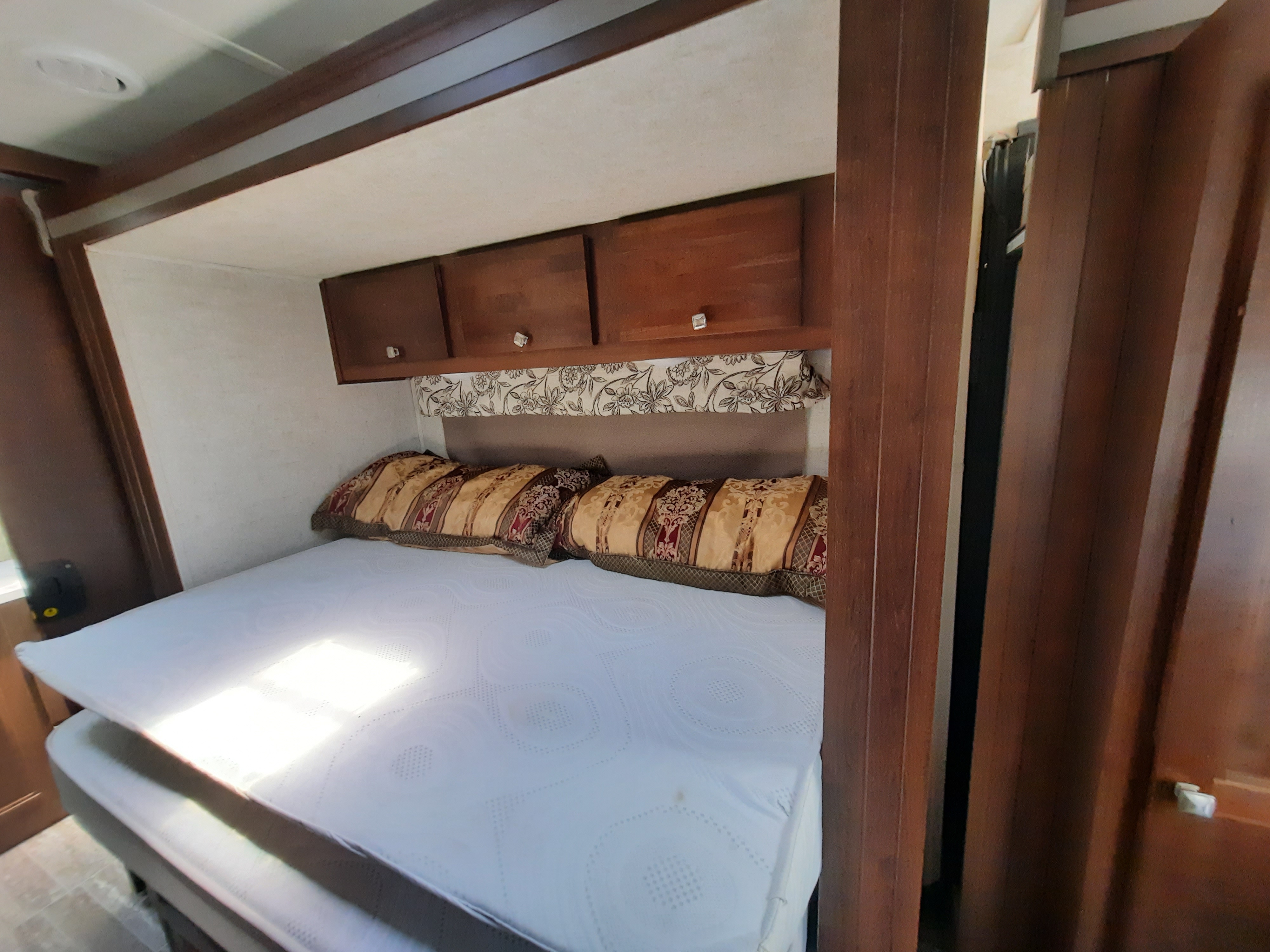 Inside this RV rental, a cozy bedroom featuring a white mattress, patterned pillows, and wooden overhead cabinets.. Forest River Other 2018