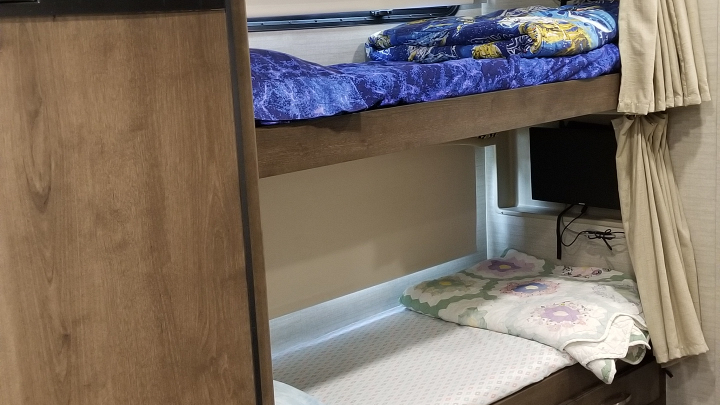 RV rental bunk beds, perfect for family travel. Cozy sleeping area with TV and privacy curtains inside an RV.. Jayco Alante 2018