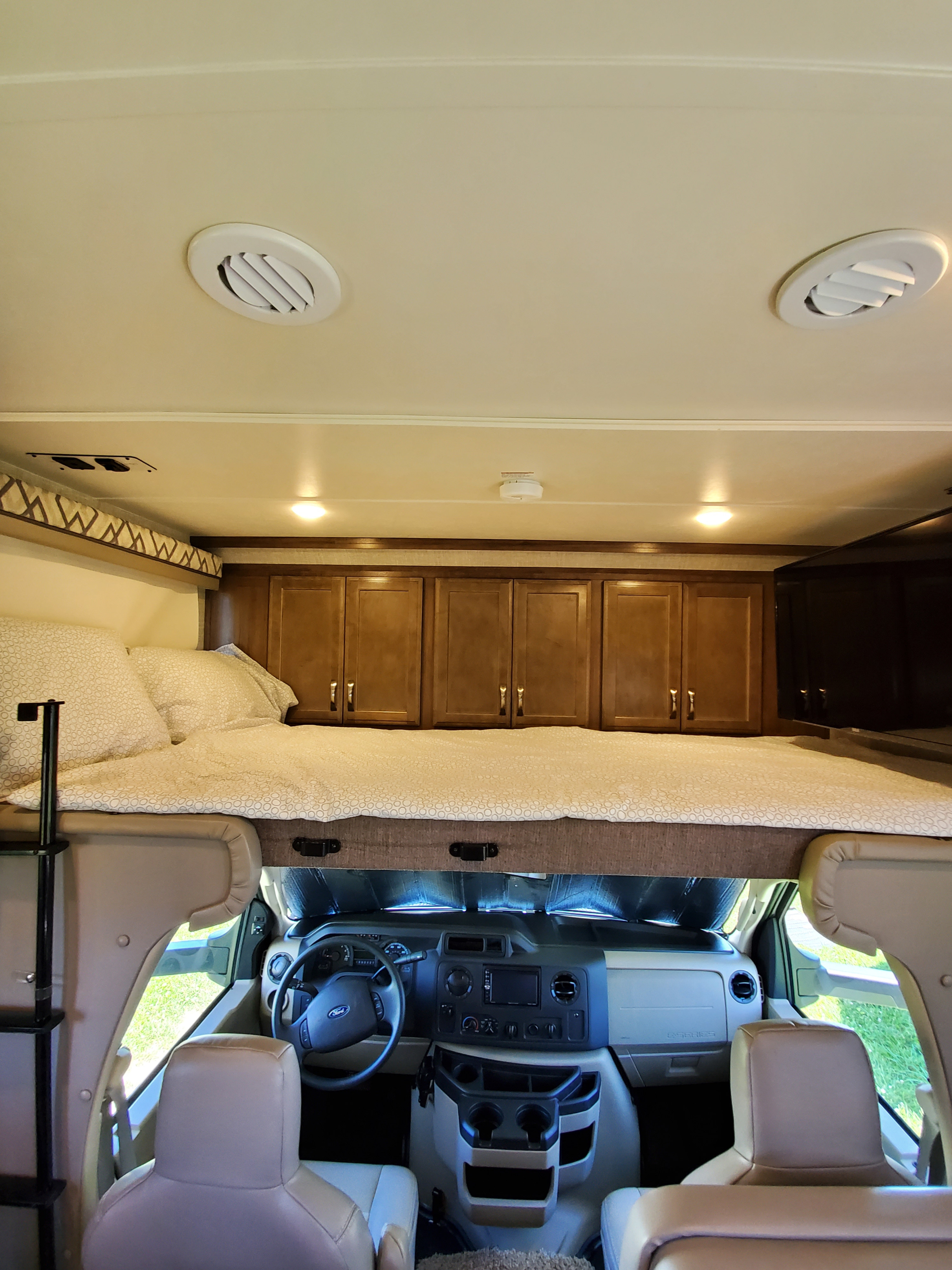 Spacious RV rental interior featuring a bed over the cab, dashboard, and front cabin seats. Ideal for travel.. Gulf Stream Conquest 2020