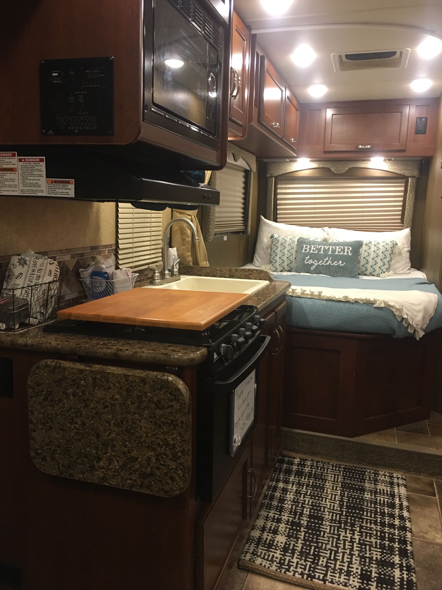 Thor RV rental interior: kitchen with stove & sink, cozy bed with "BETTER together" pillow, warm lighting.. Other Other 2017