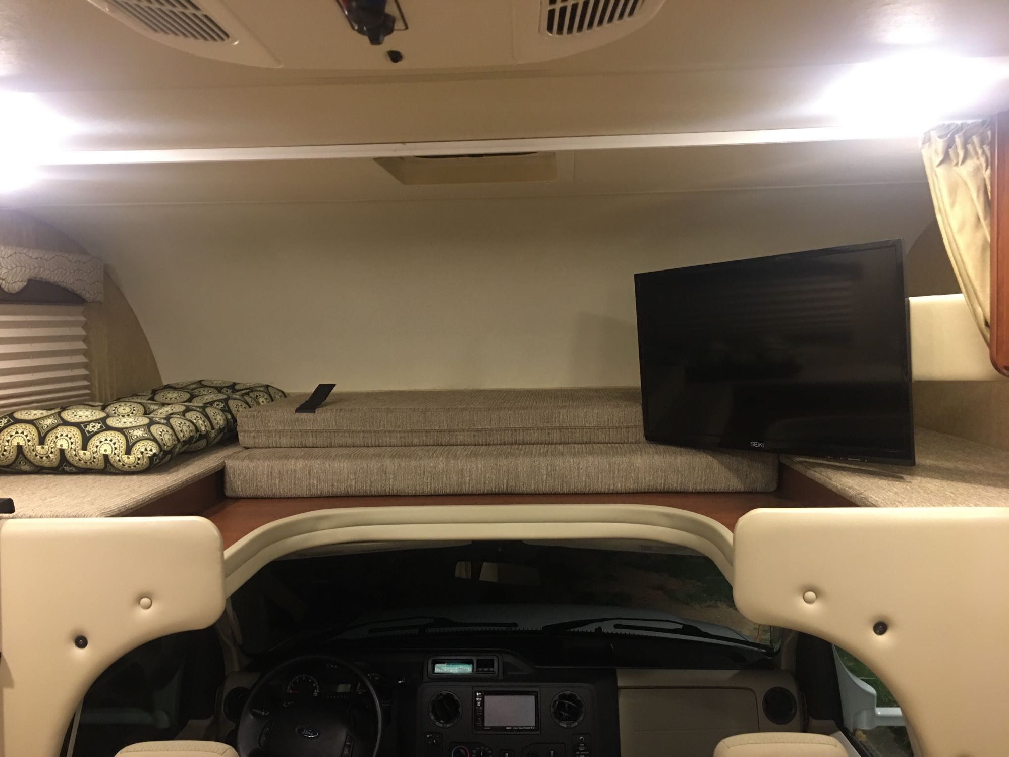 Inside an RV rental, featuring a comfortable cab-over bunk with a TV above the driver's dashboard.. Other Other 2017