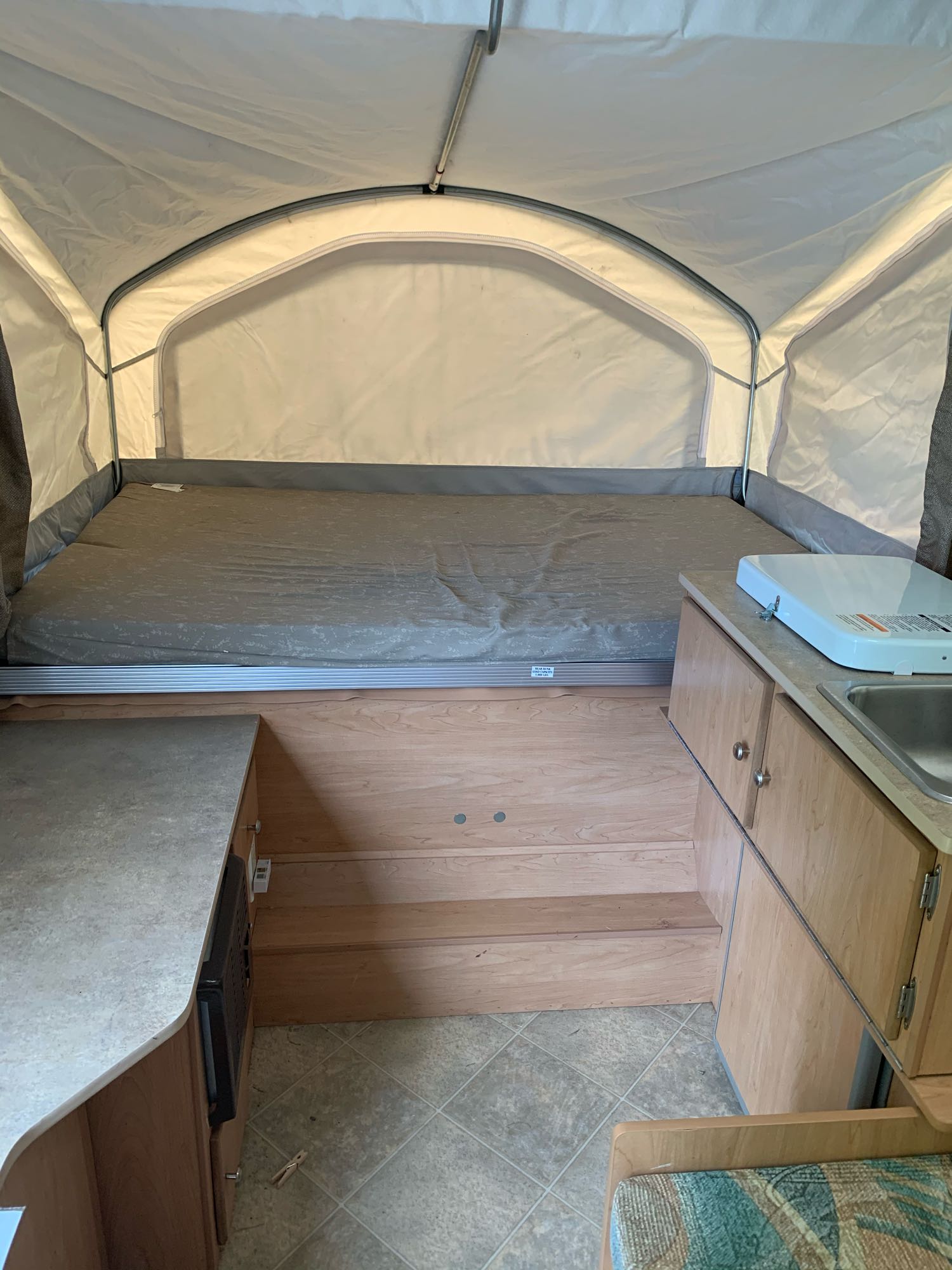 RV rental pop-up camper interior: extended bed, small kitchen with sink/stove, and wooden steps. Compact & functional.. Coachmen Sport 2007