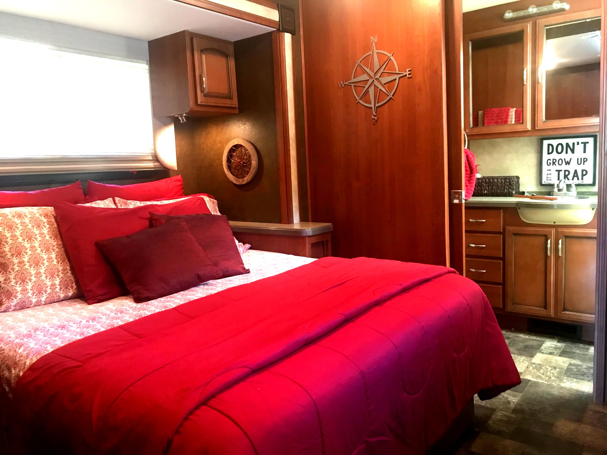 Spacious RV rental bedroom featuring a vibrant red bed, wood cabinetry, and a cozy sink area. Perfect for a comfortable journey.. Fleetwood Class A 2015