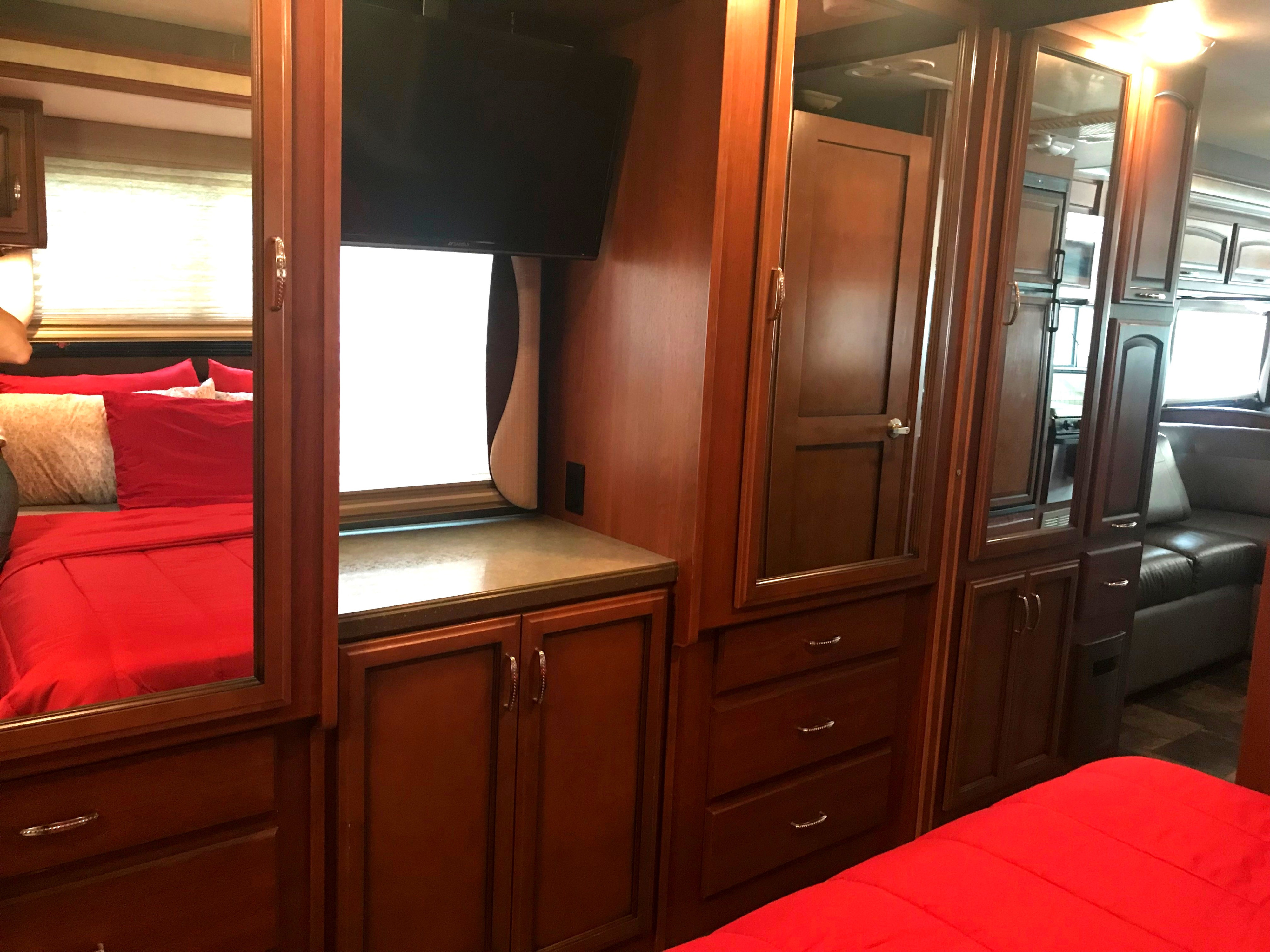 RV rental bedroom with vibrant red bedding, a TV, and mirrored storage reflecting the kitchen/living area.. Fleetwood Class A 2015