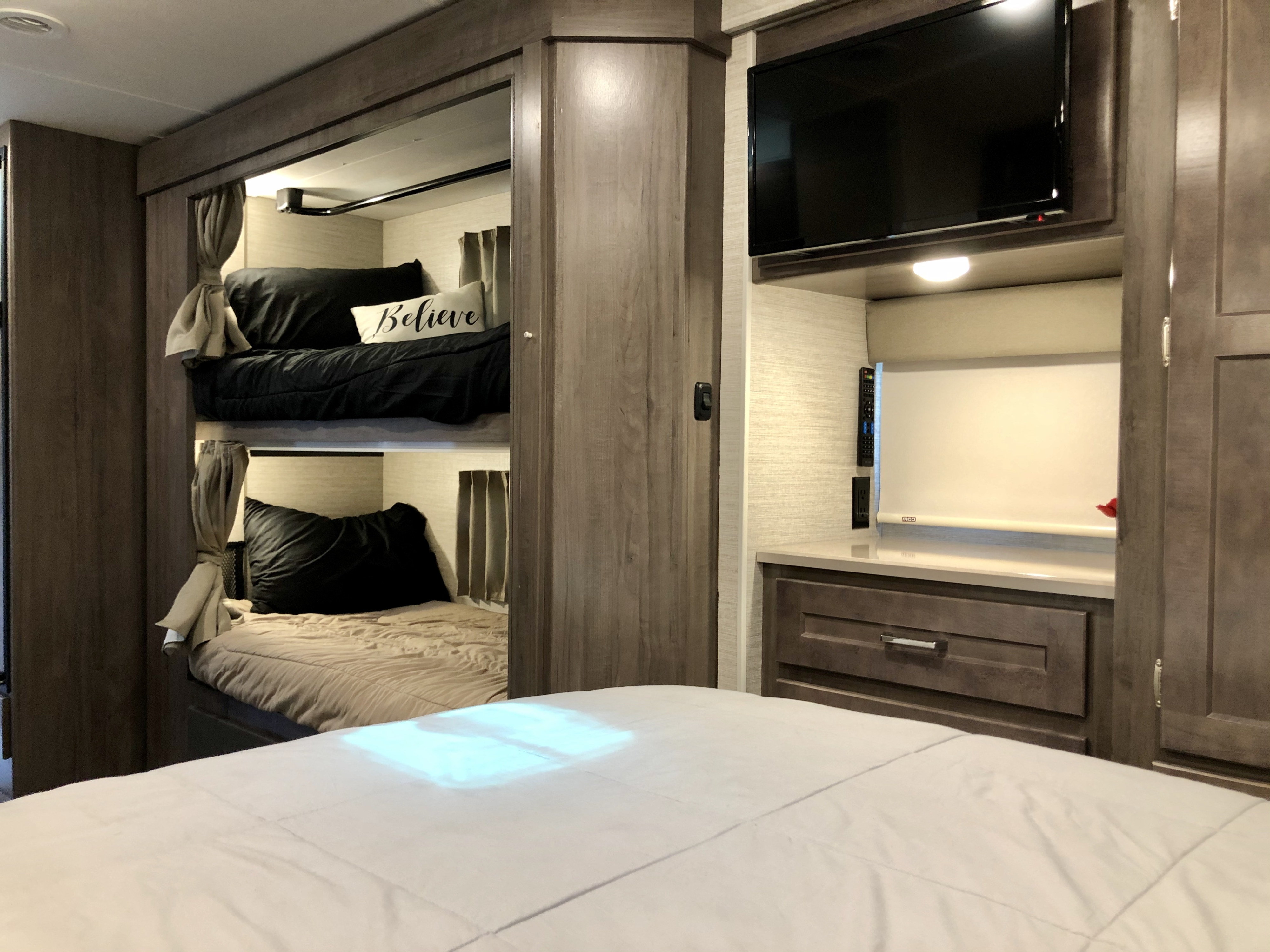 Cozy rv rental interior featuring bunk beds, a mounted TV, and a comfortable main bed. Perfect for family trips.. Winnebago Minnie Winnie 2020