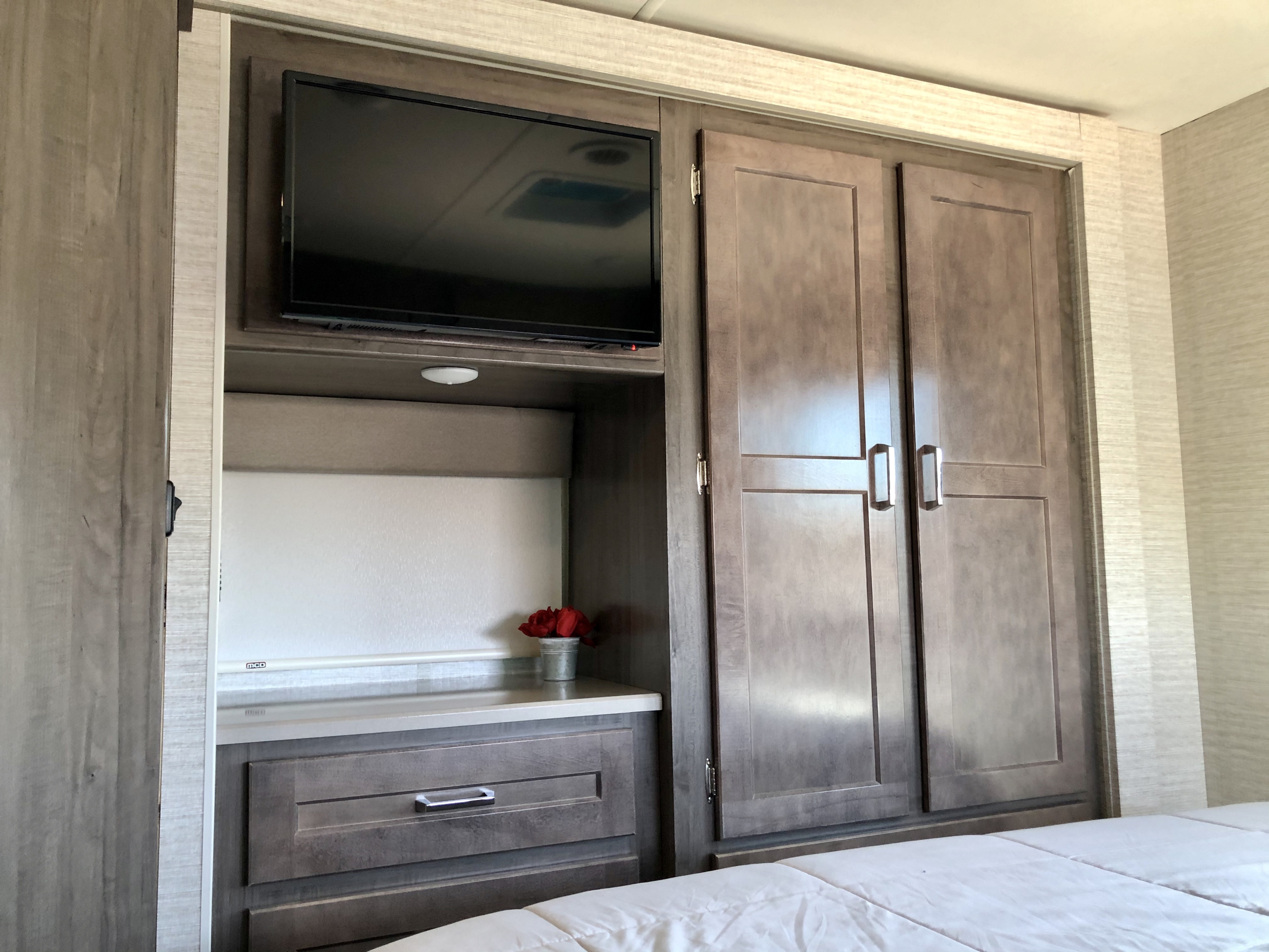 Comfortable RV rental bedroom interior featuring a mounted TV, ample storage in a built-in closet, and a handy nightstand.. Winnebago Minnie Winnie 2020