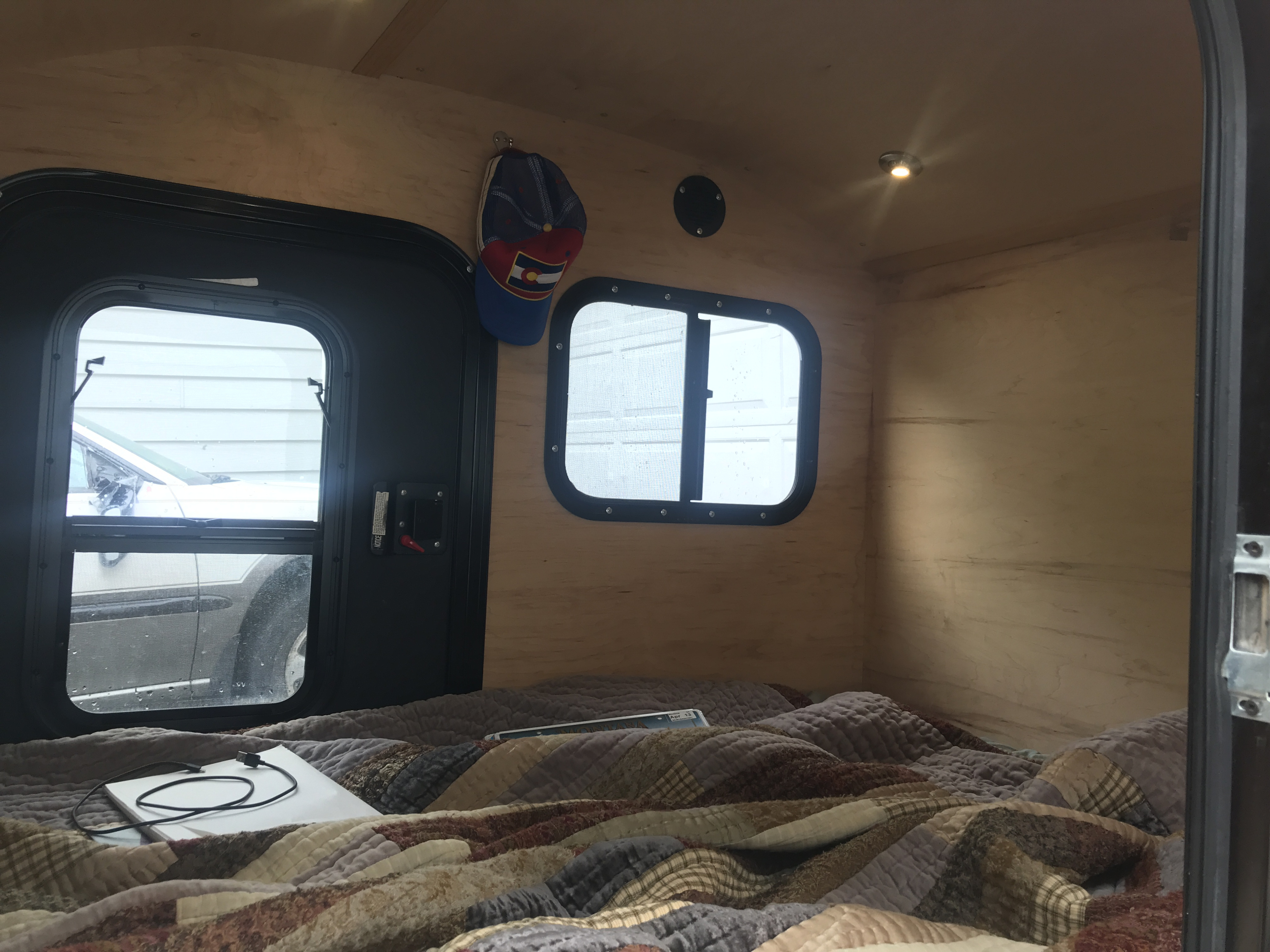 Cozy RV rental camper interior with light wood walls, comfy bed, two windows, and a hanging hat.. TC Teardrops 4x8 custom 2015
