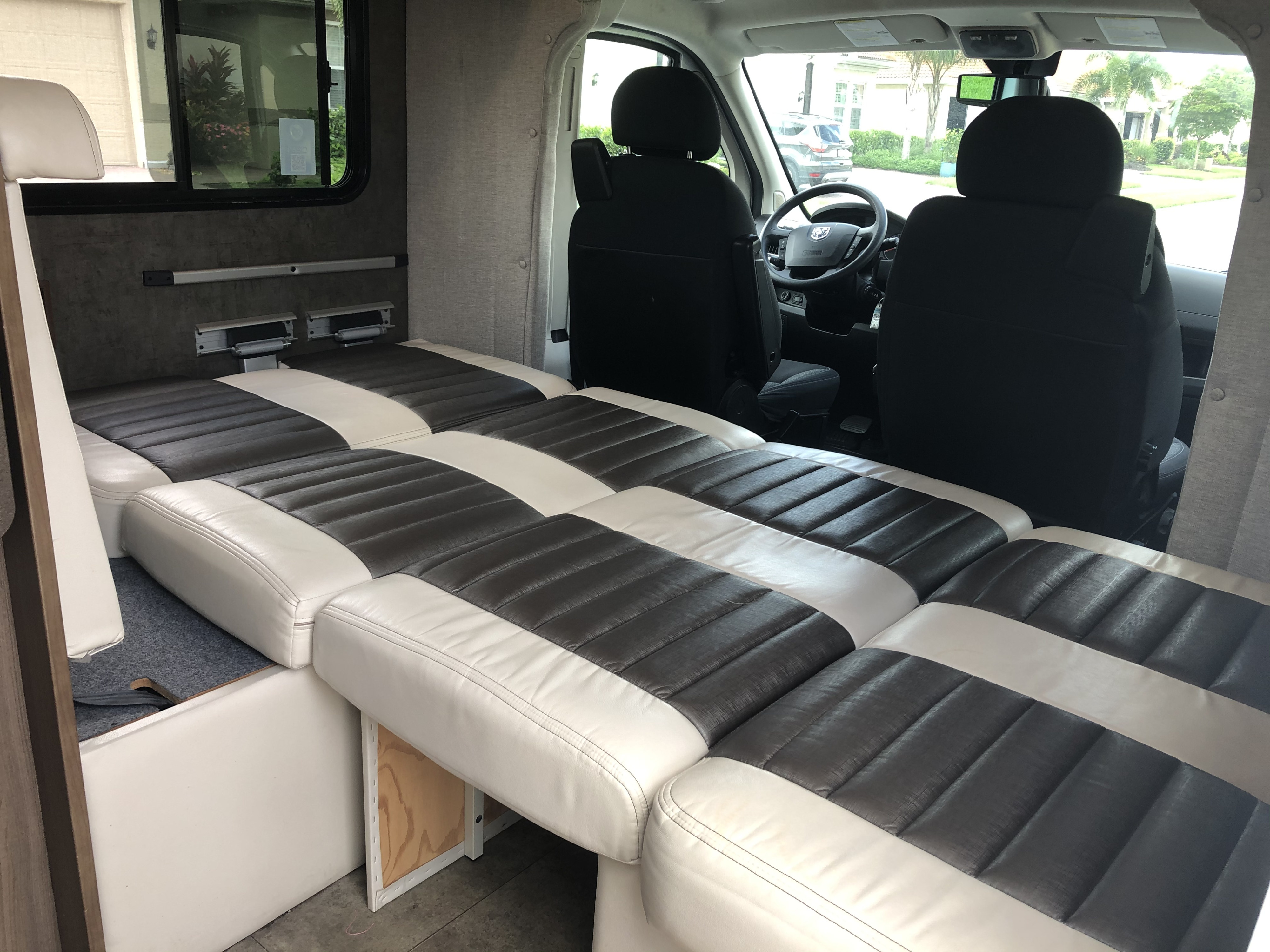 RV rental's comfortable interior: modular white and dark grey cushions convert into a bed, with the driver's cabin visible.. Winnebago Trend 2015