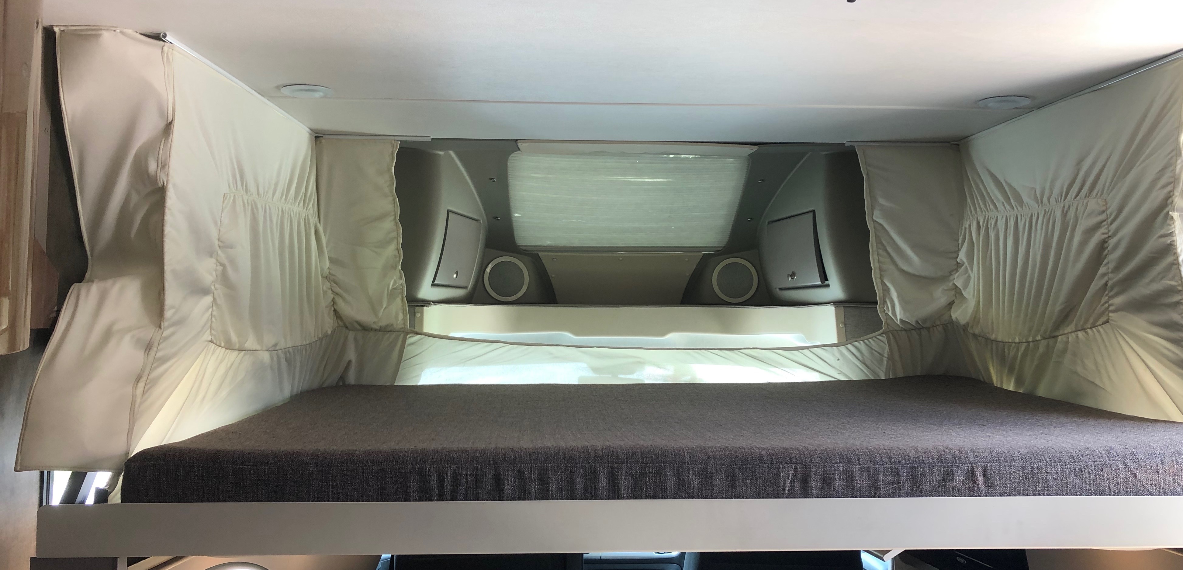 RV rental: Cozy bunk bed area featuring a grey mattress, light privacy curtains, and overhead storage with window.. Winnebago Trend 2015