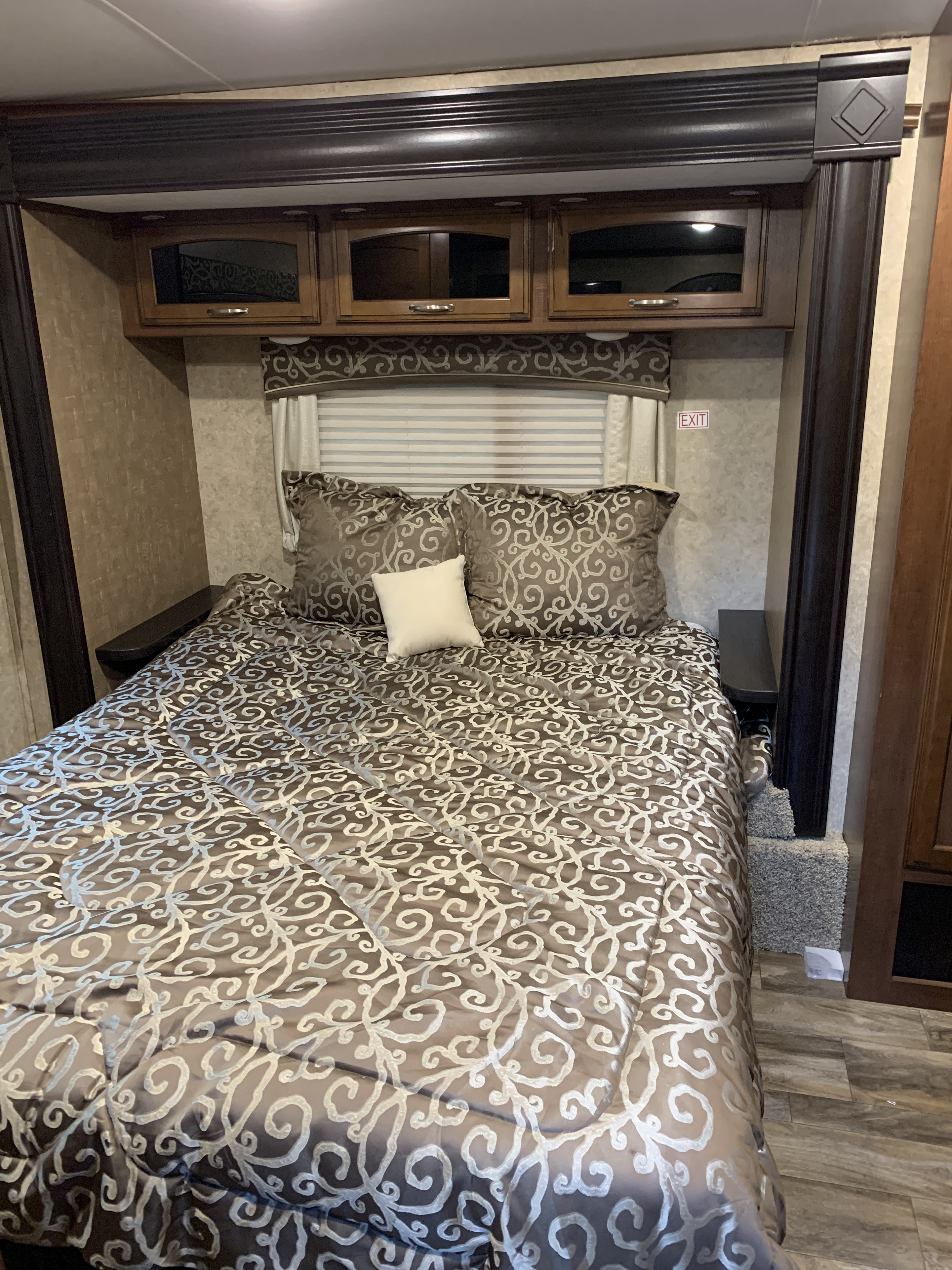 This RV rental bedroom features a comfy bed with intricate patterned bedding, overhead cabinets, and convenient side shelves.. Jayco White Hawk 2017