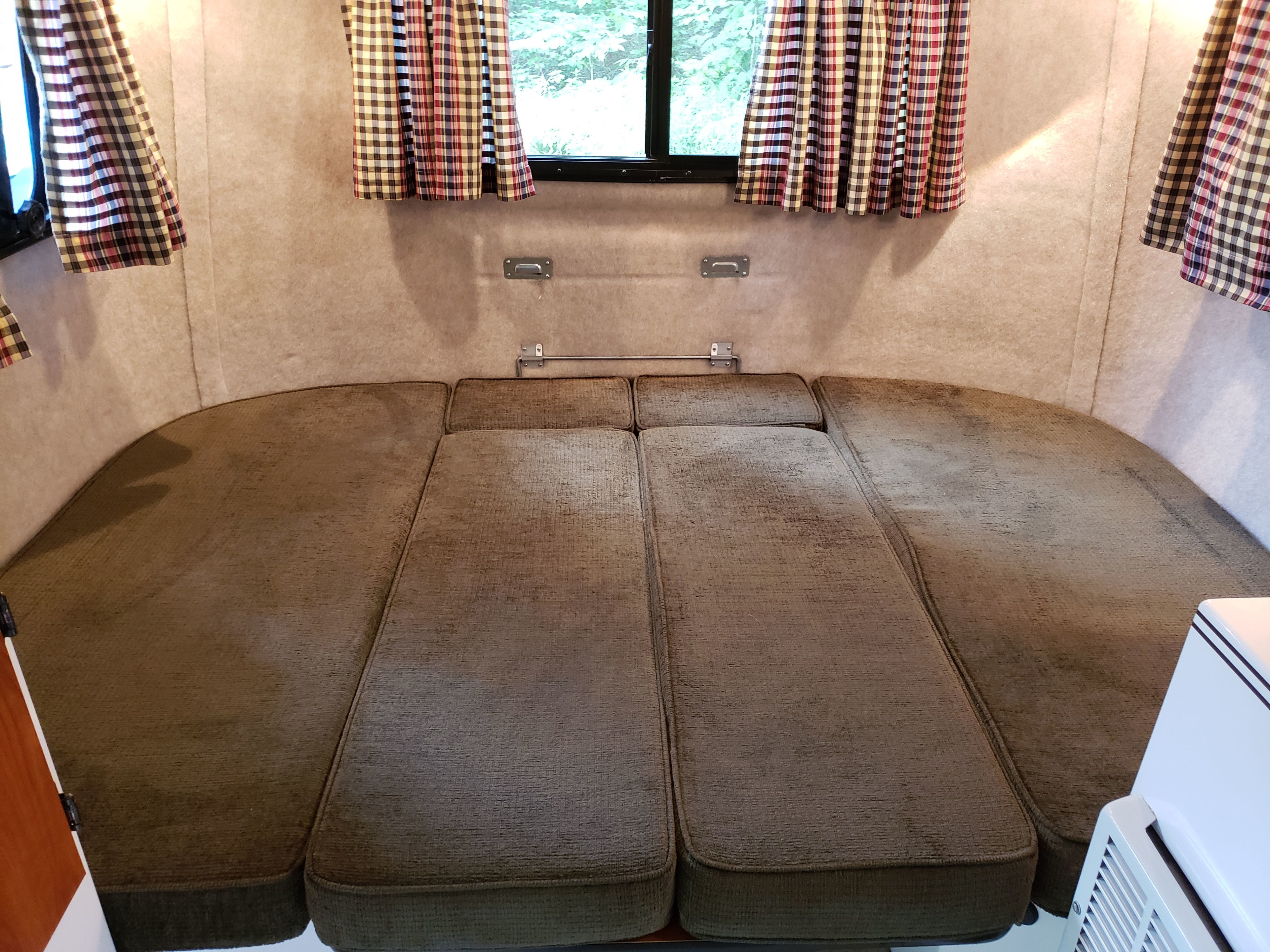 RV rental interior: Comfortable olive-green cushions forming a bed, with plaid curtains at windows.. Scamp Scamp Trailer 2015